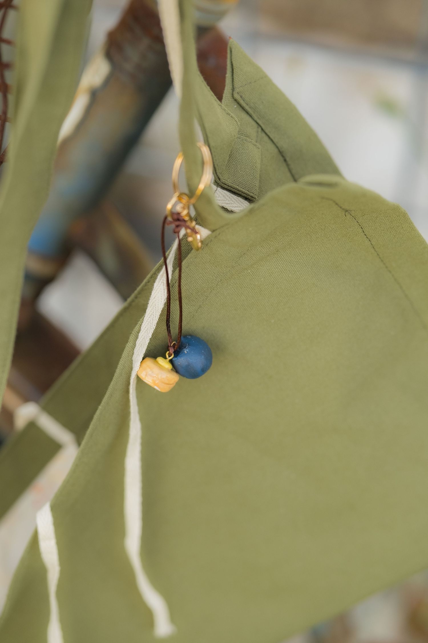 Olive green fabric bag with blue bead and wooden charm hanging from ribbon on decorative display.
