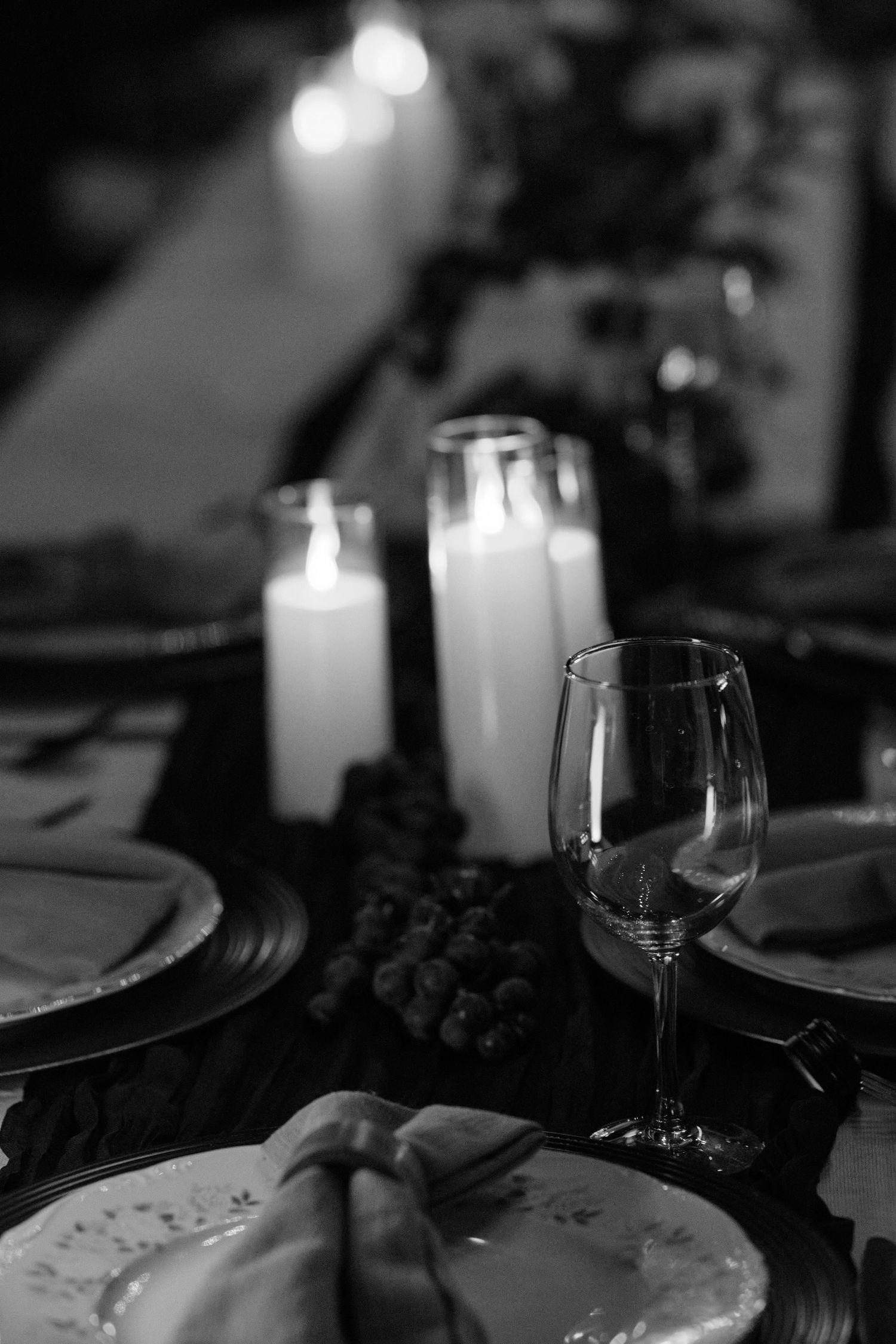 Black and white table setting with lit candles, wine glass, and plates creating an intimate dining atmosphere.