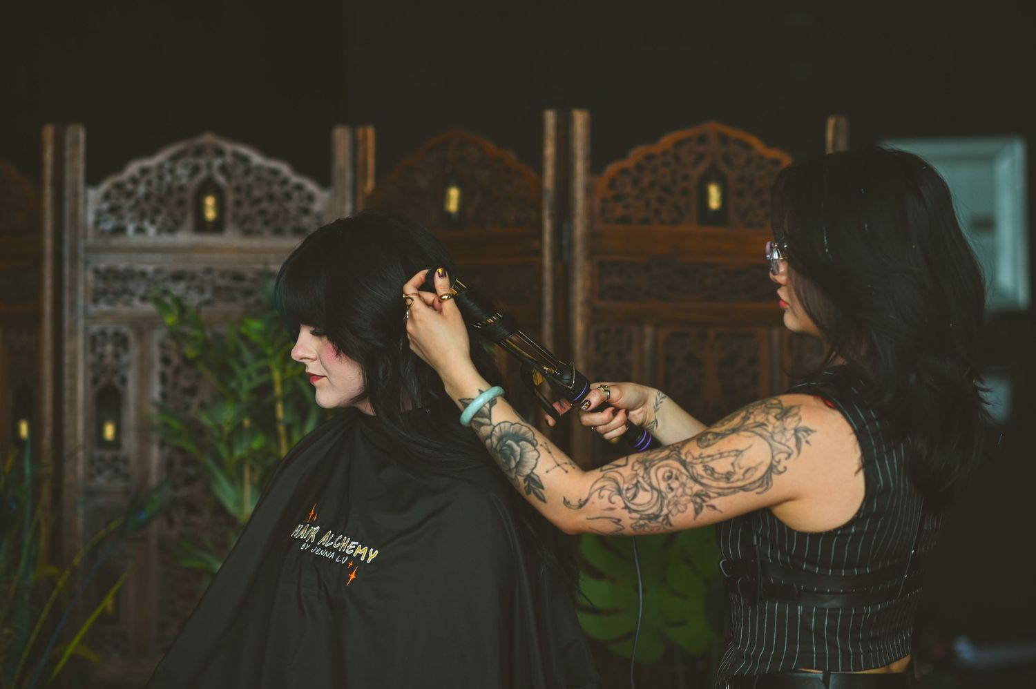 Tattoo artist works on a detailed arm piece in a dimly lit professional studio setting.