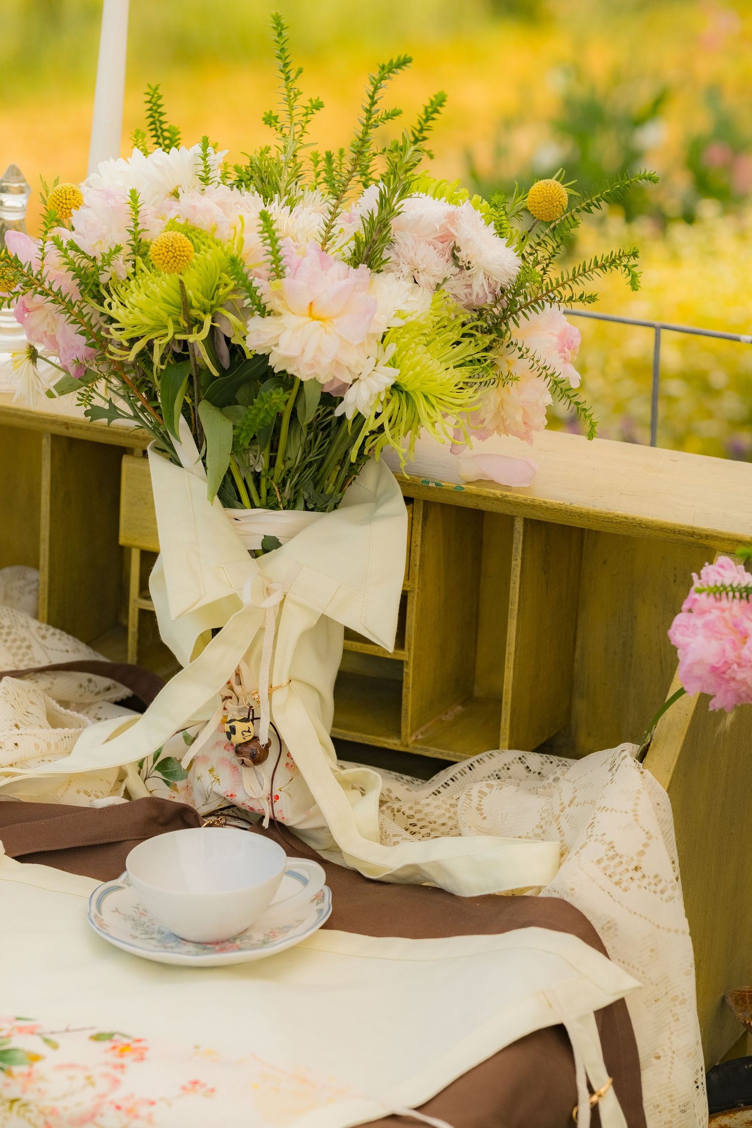 Elegant outdoor table setting with pink floral arrangement, lace cloth, and teacup in a garden.