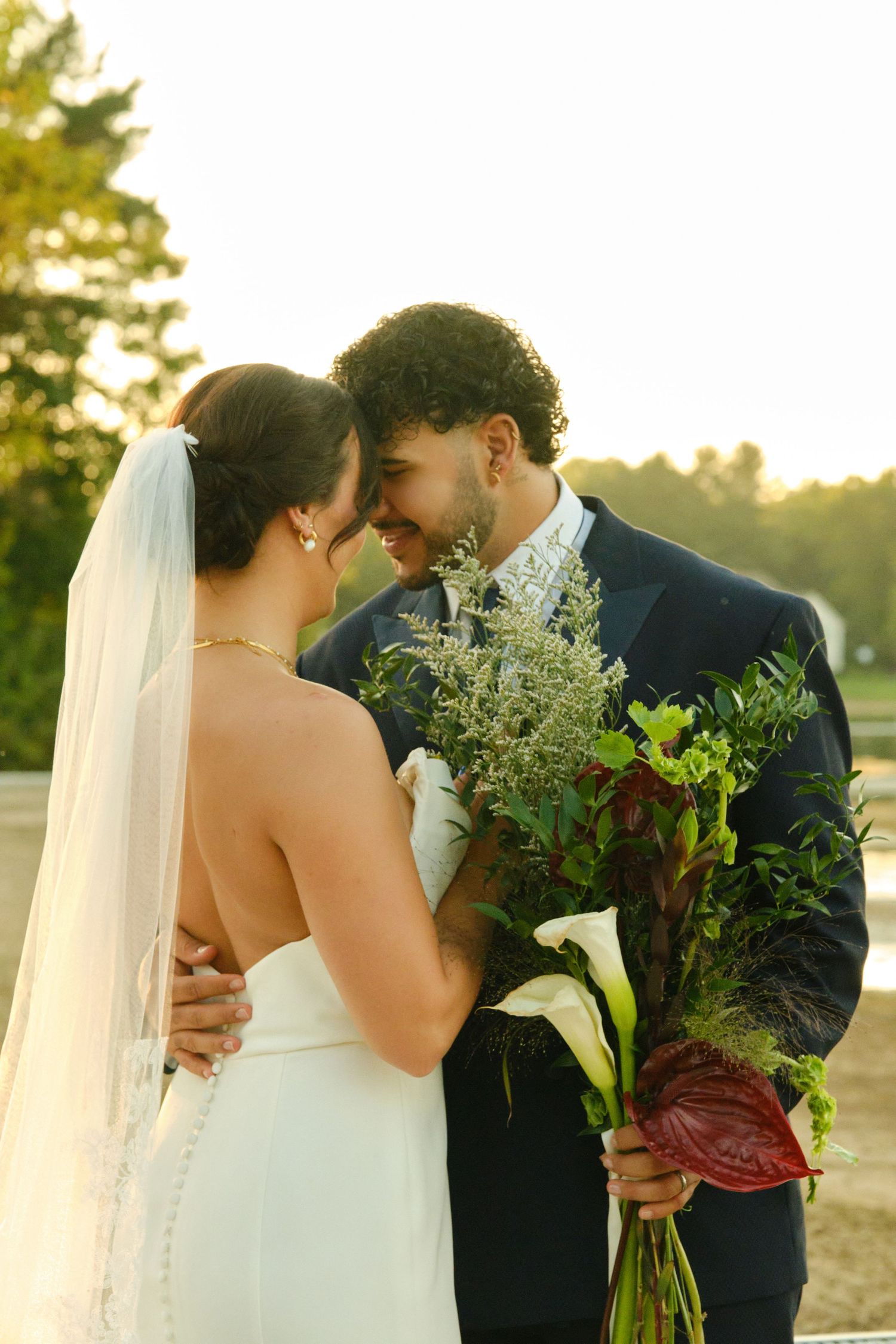 A tender moment between newlyweds at sunset, with the bride in white and a beautiful bouquet of calla lilies and greenery.