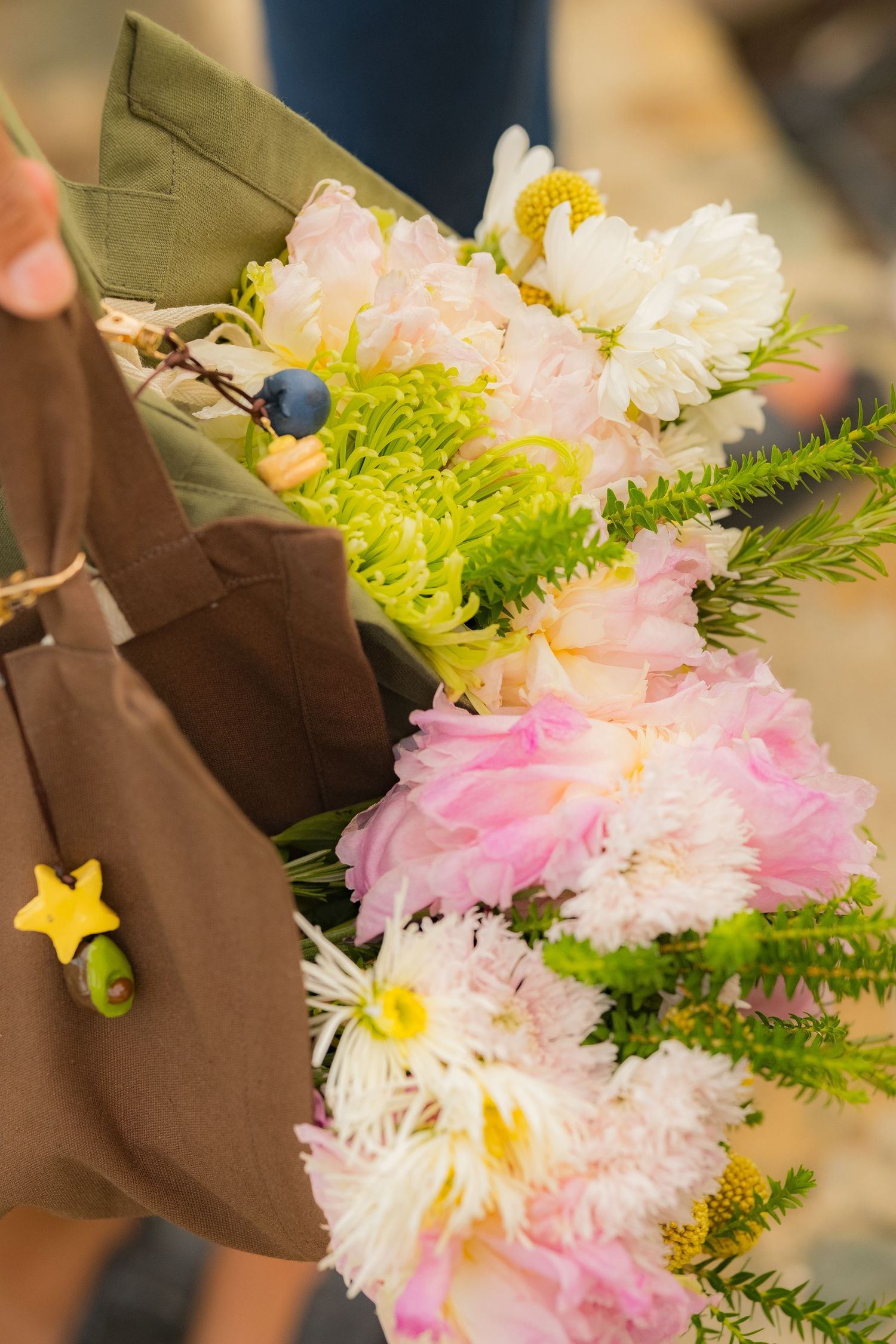 Close-up of a brown tote bag holding a vibrant bouquet of pink peonies and white chrysanthemums.