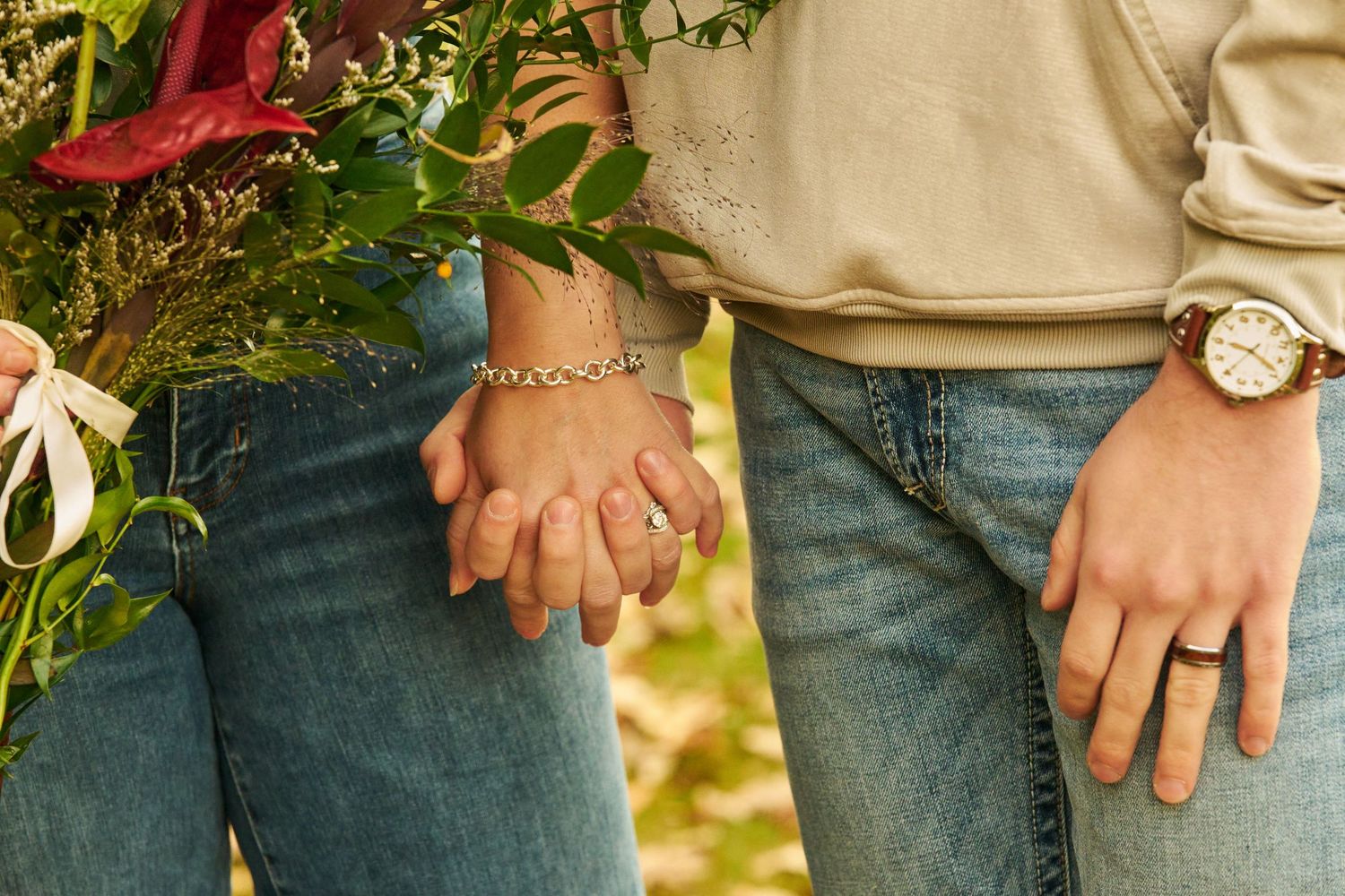 Close-up of hands wearing wedding rings while holding a floral bouquet.