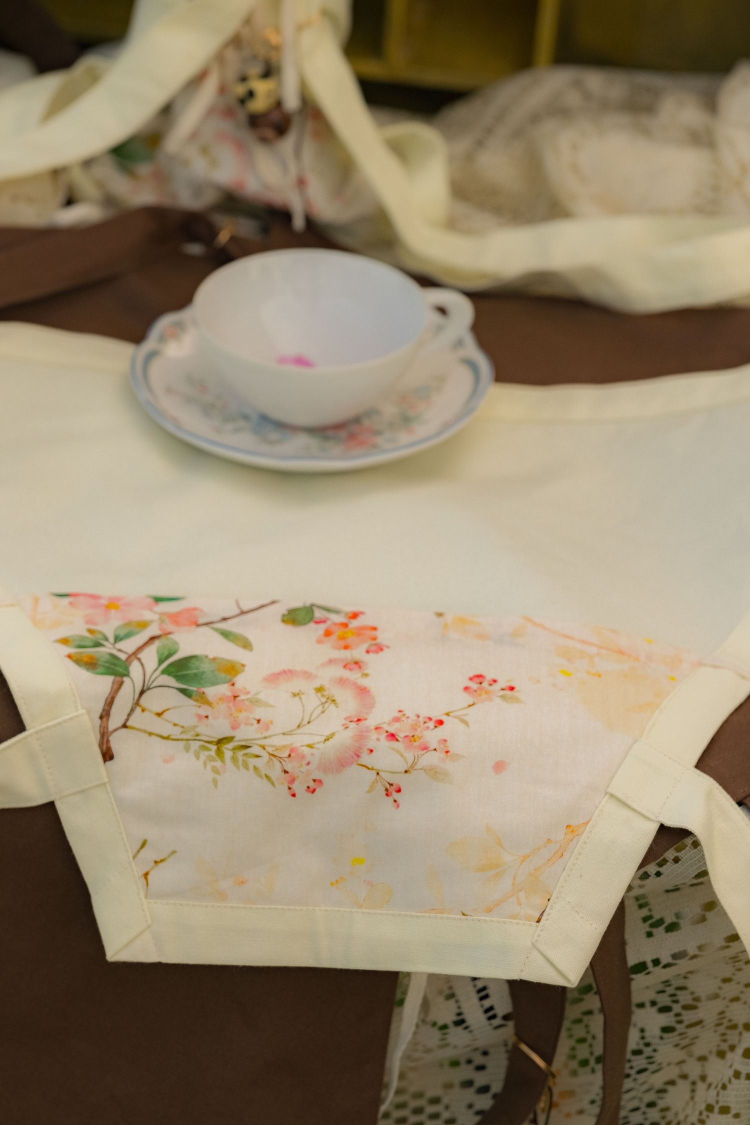 Floral printed fabric tote bag laid flat on a table with a decorative teacup and saucer in the background.