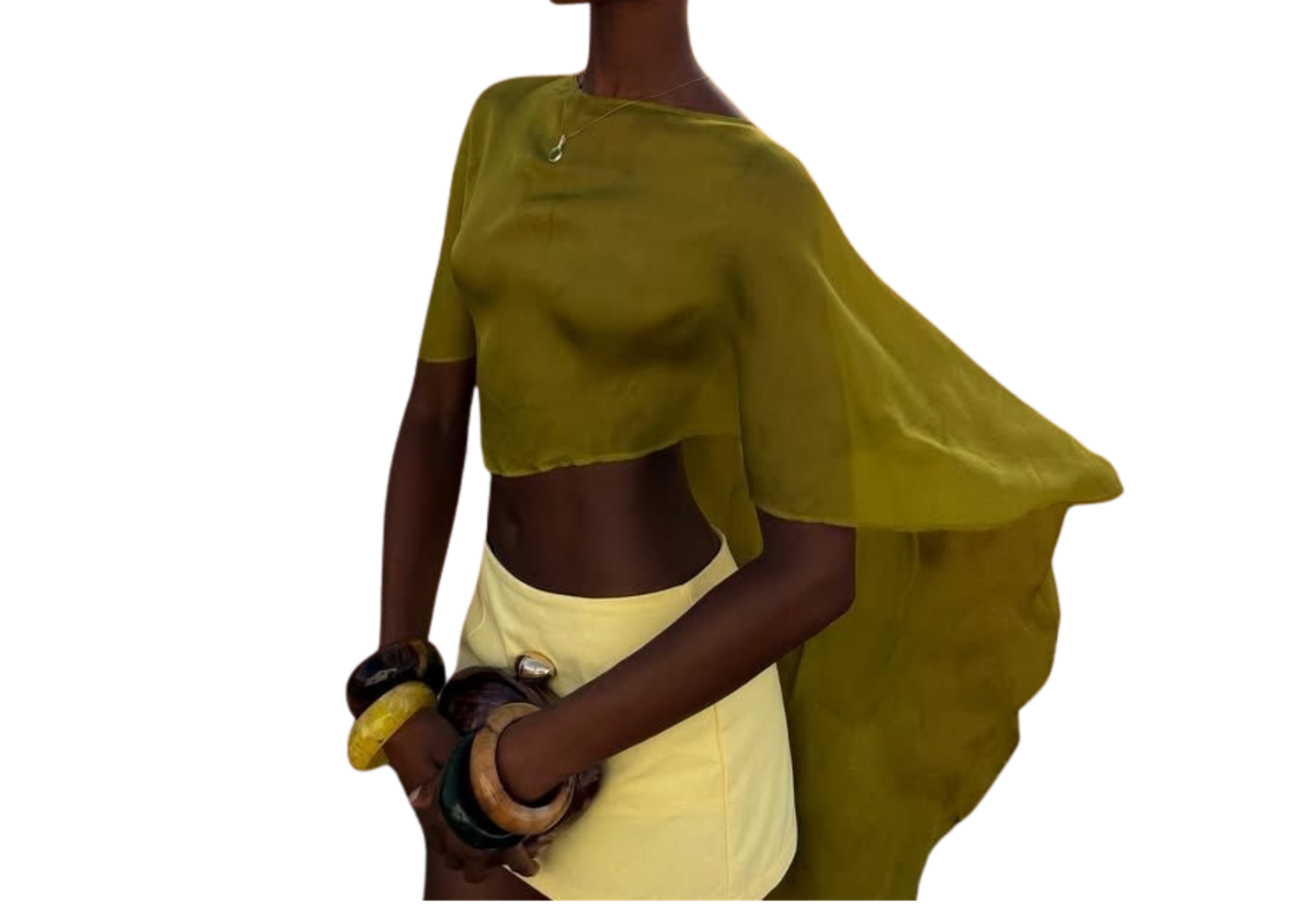 Woman wearing an olive green sheer cape top and cream skirt, accessorized with chunky bangles, on white background.