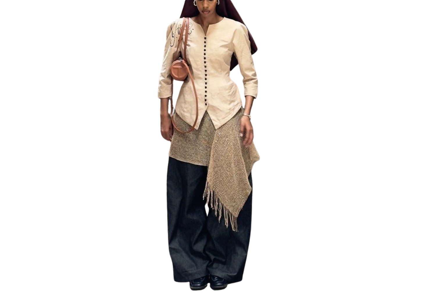 Woman wearing a beige button-up jacket with fringed wrap skirt and dark wide-leg pants.