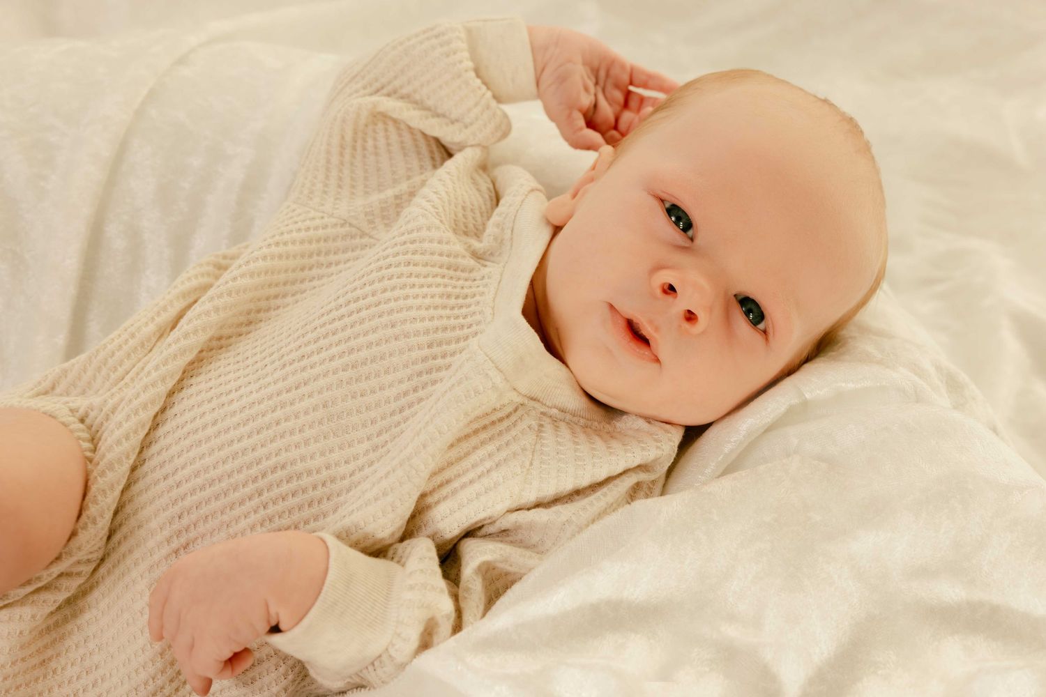 Peaceful baby in cream-colored outfit resting on white linens.