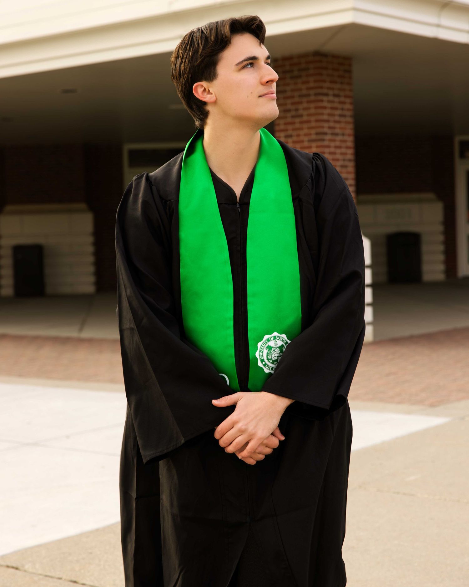 Graduate wearing black gown and bright green stole poses for portraits outside building.