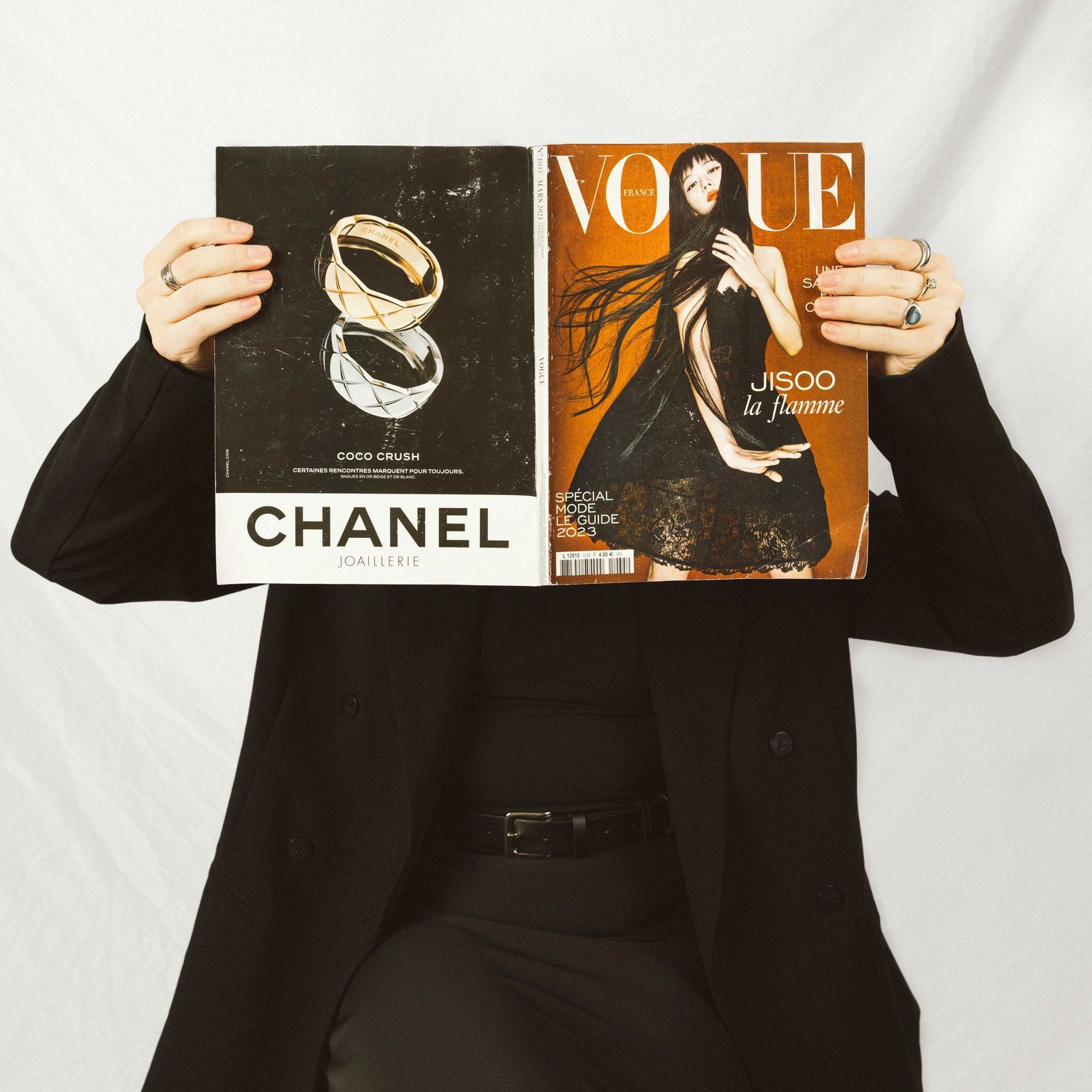 Fashion magazines and Chanel products artfully arranged on white background with hands holding items.