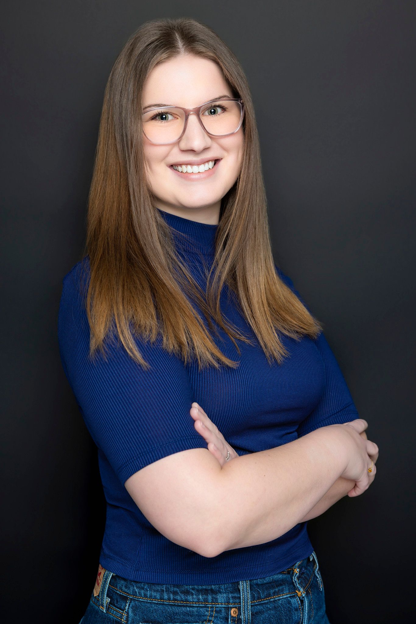 Professional headshots in blue turtleneck and jeans against dark studio backdrop.