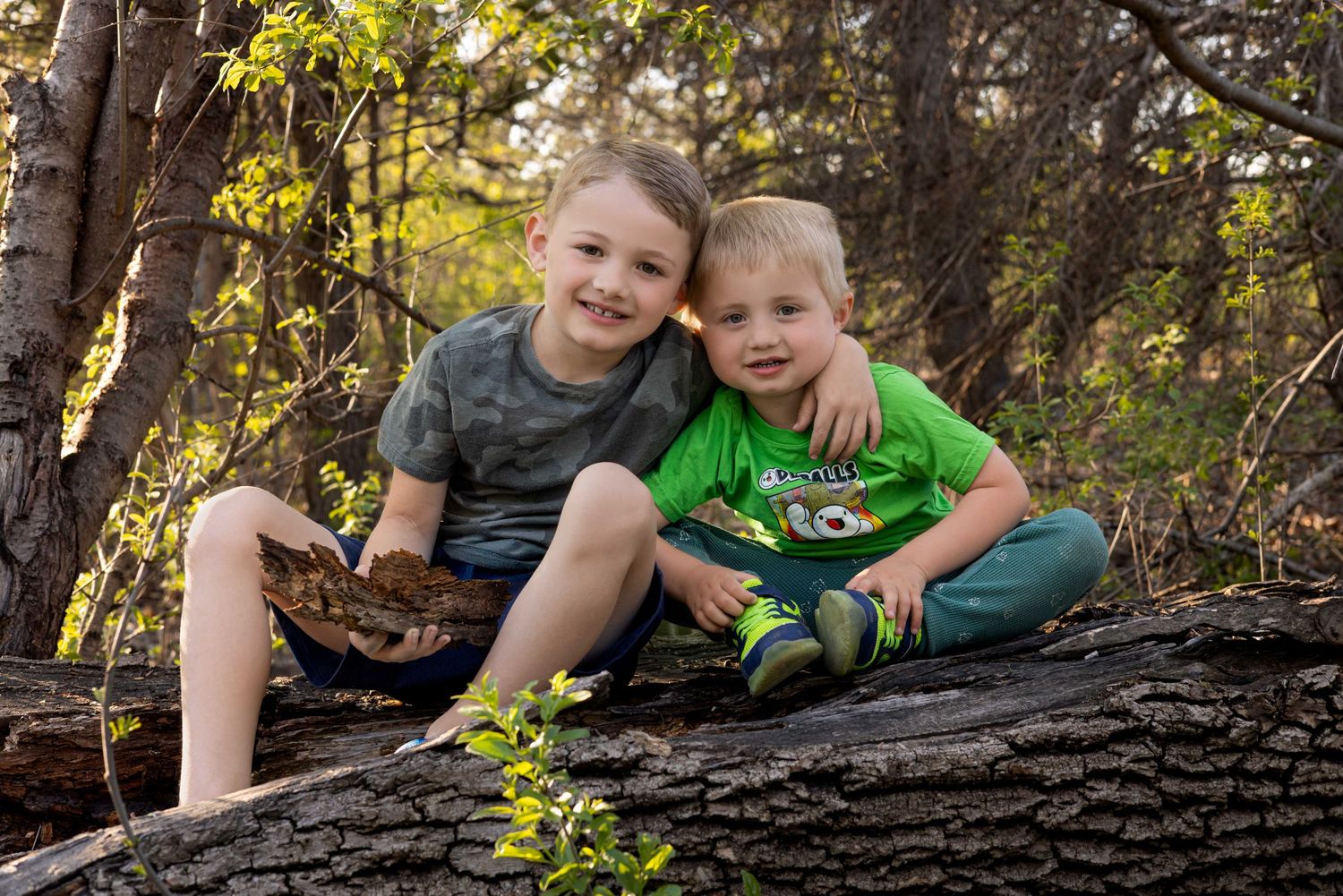 Family playfully poses on fallen tree trunk in autumn forest setting.