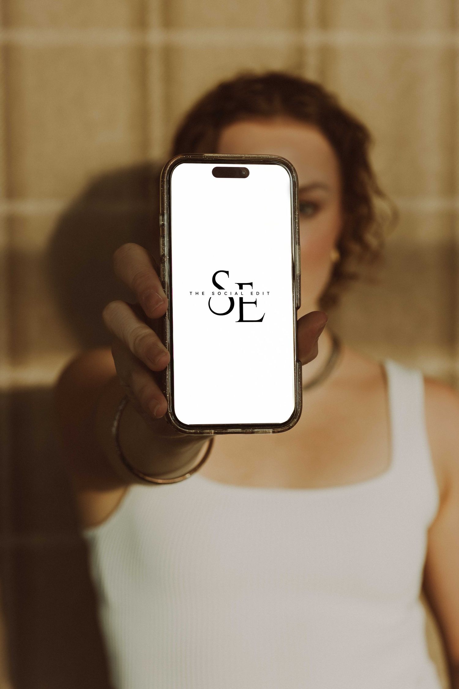 Hand holding smartphone displaying logo against warm-toned interior background.
