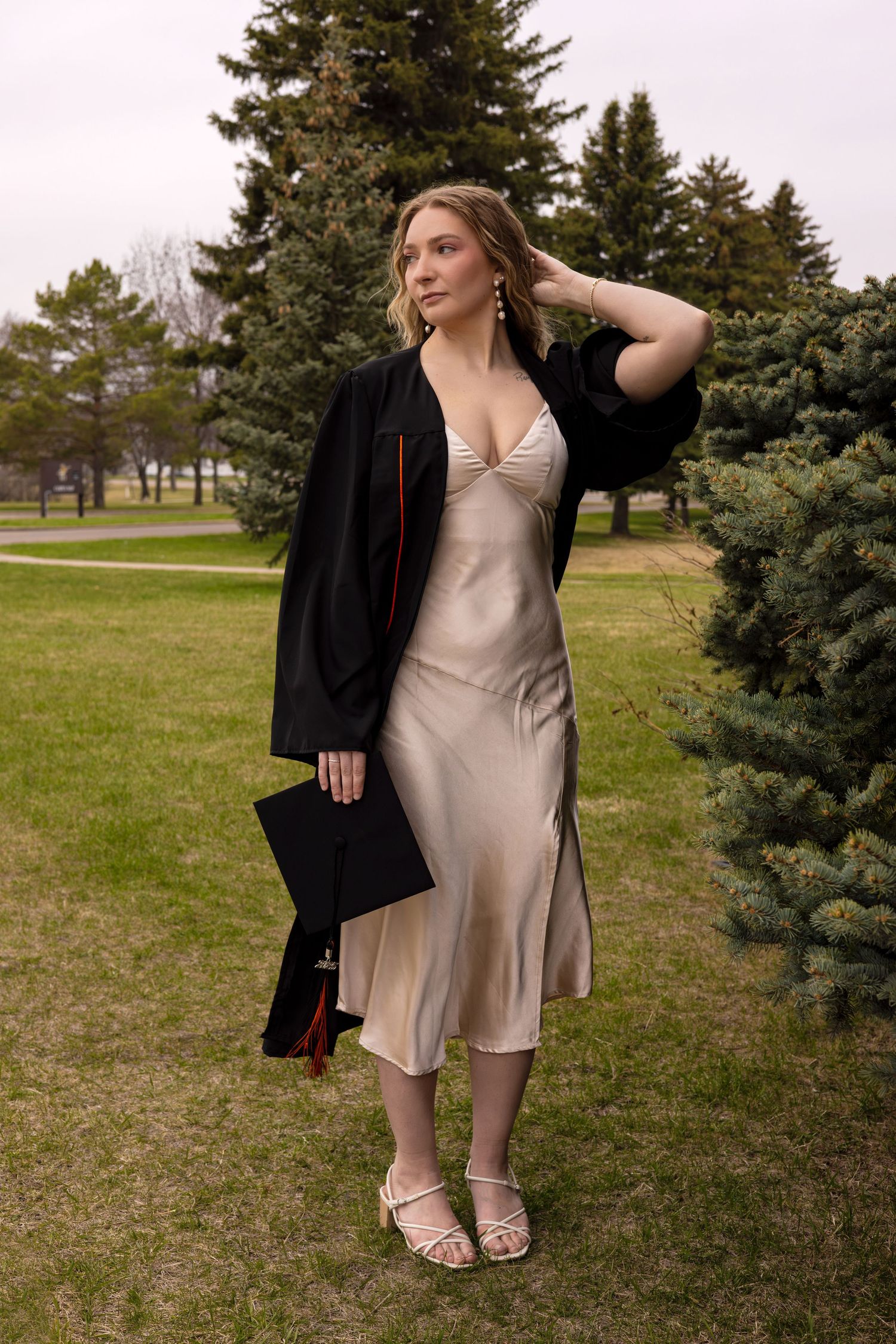 Graduation portrait session in a park with beige dress and black graduation gown.