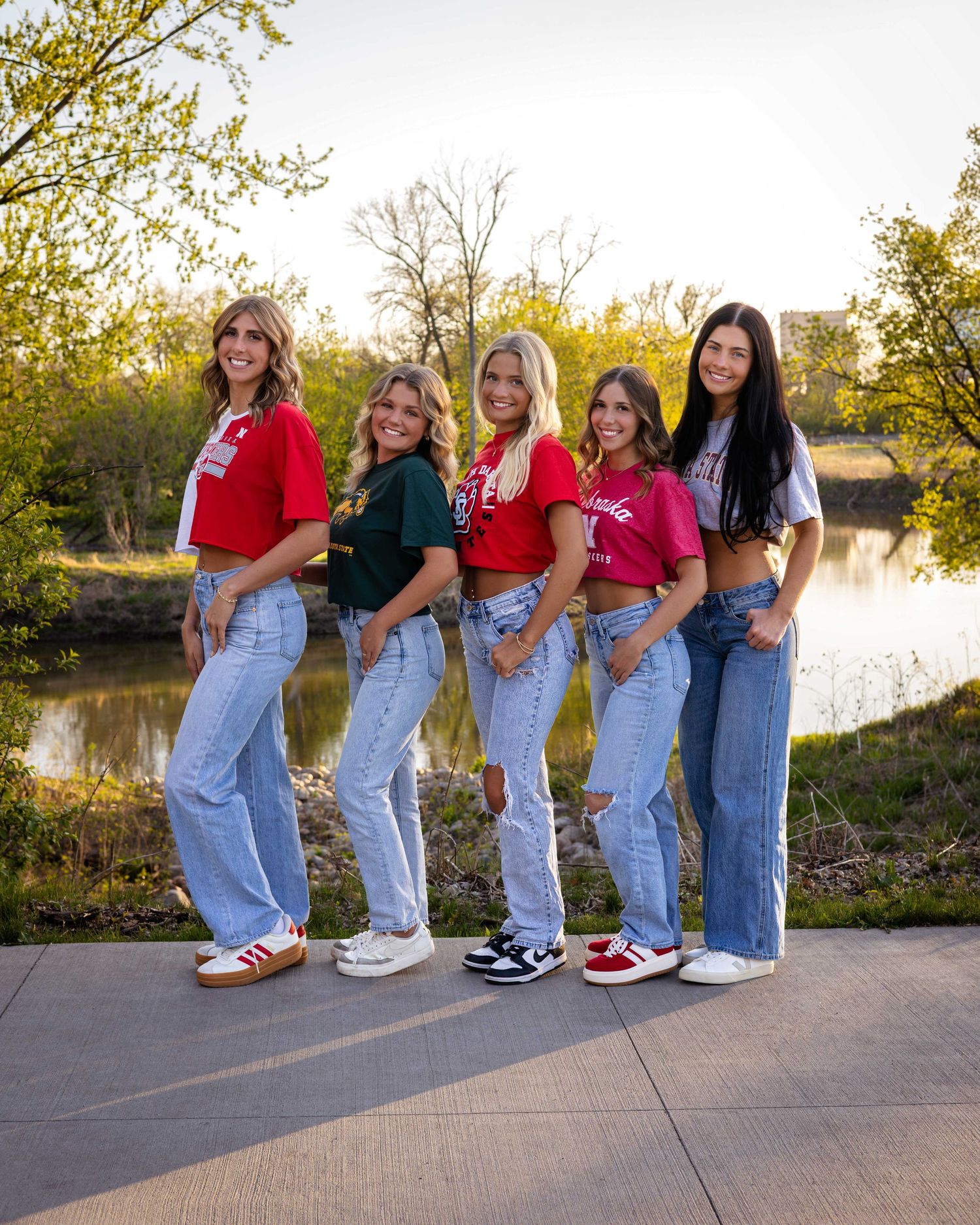 Line of people in jeans showing off colorful sneakers against outdoor backdrop.