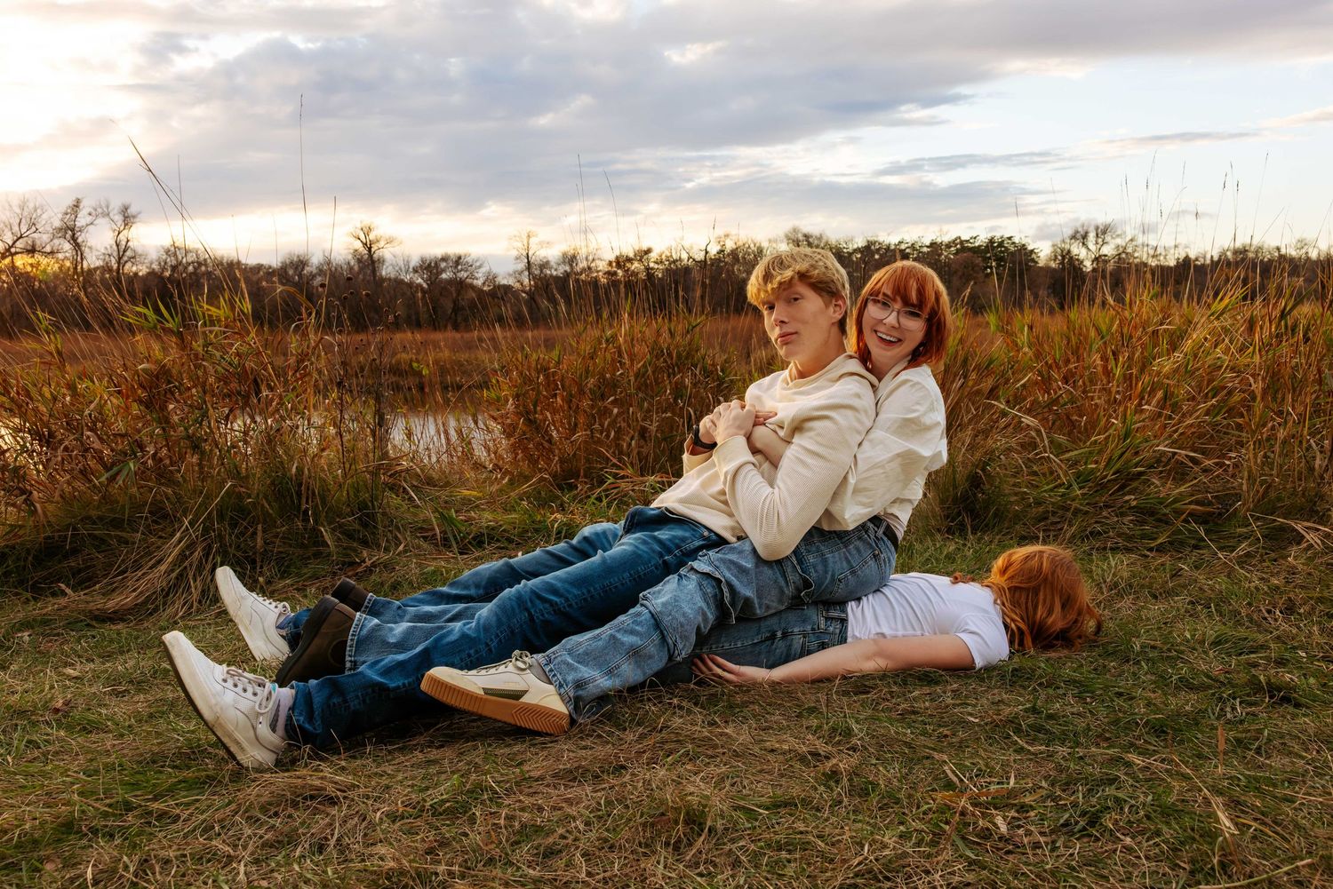 Friends in coordinated outfits lay in grass during golden hour photoshoot.