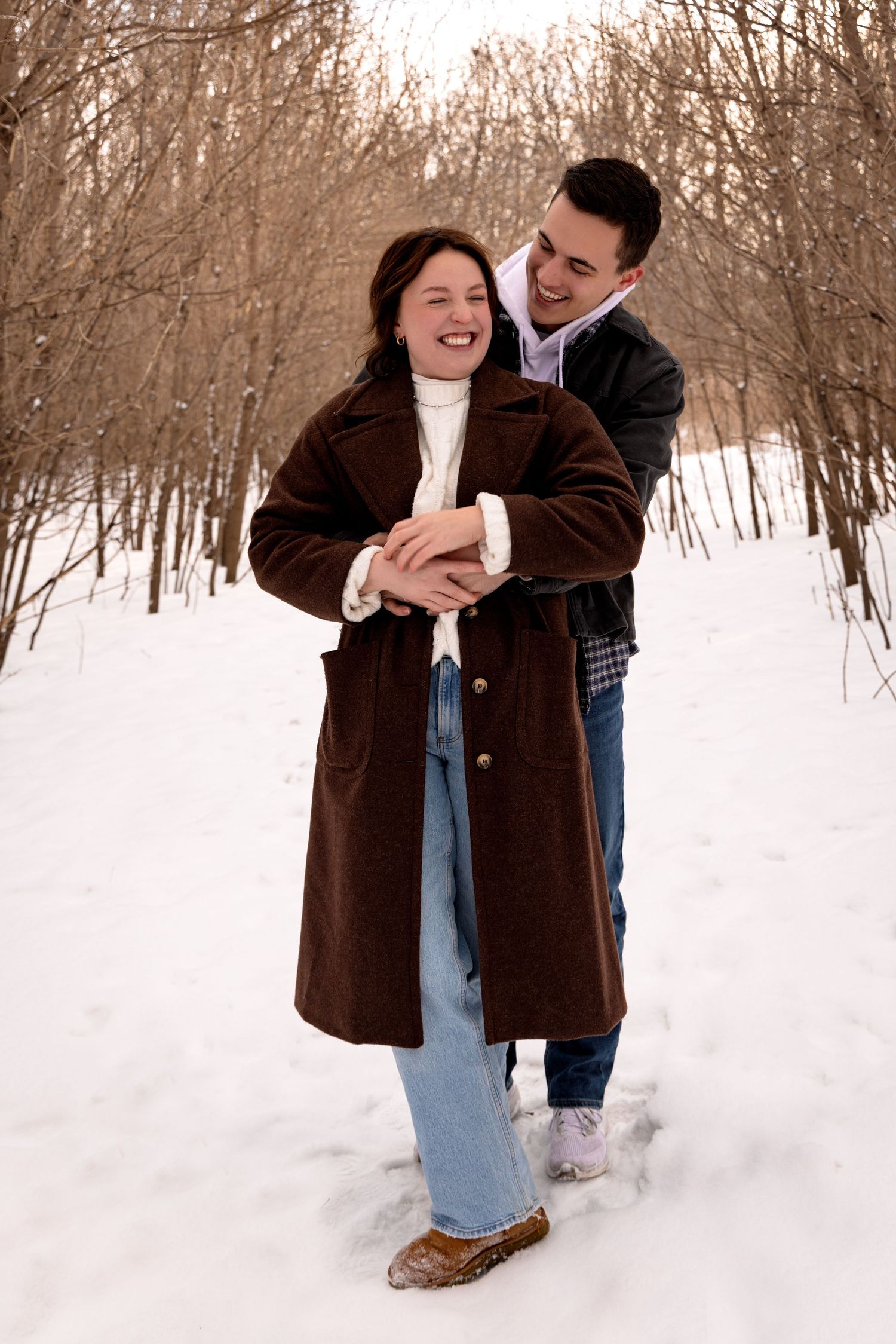Romantic winter photos of couples playing in deep snow surrounded by bare trees.
