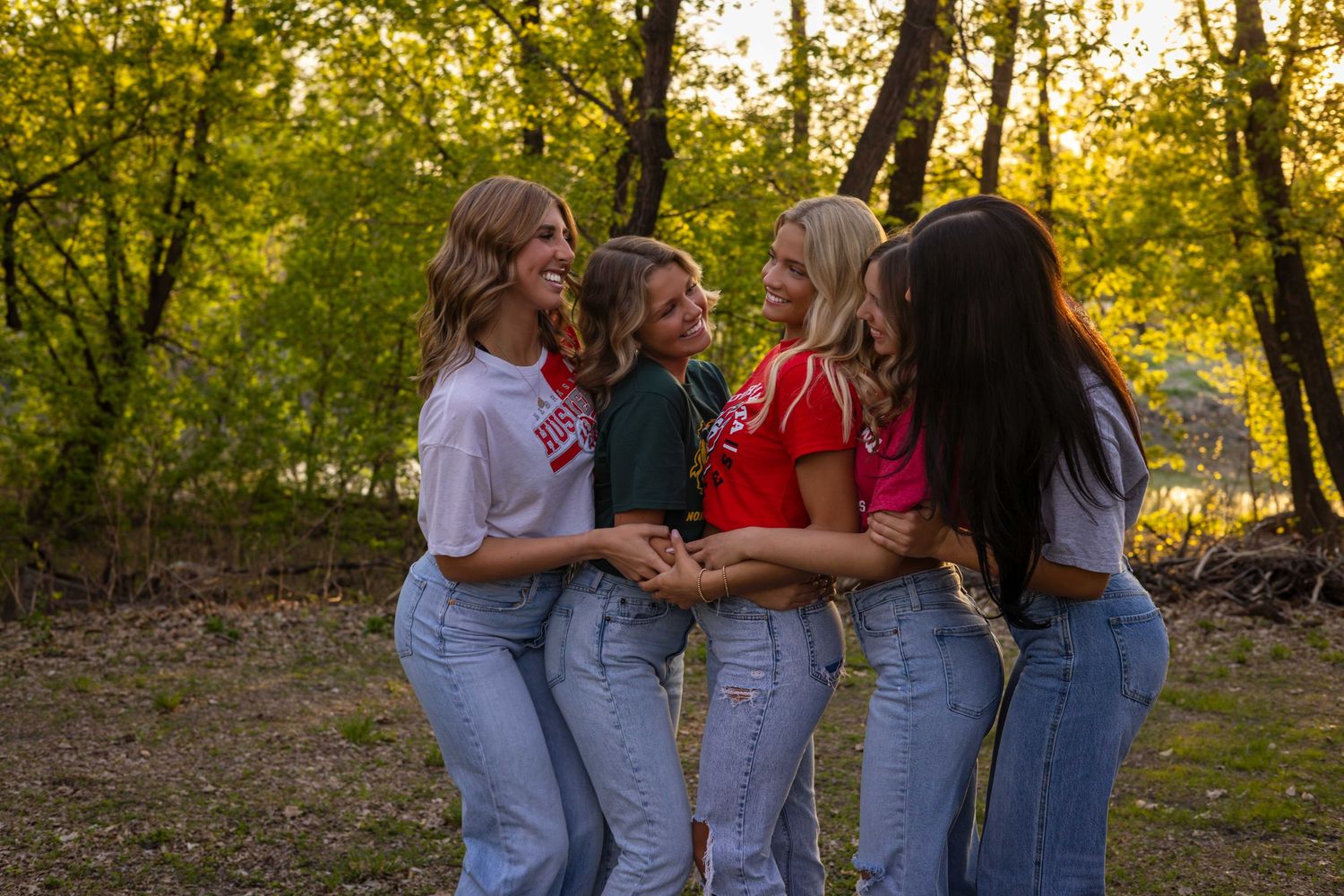 Group of friends in denim jeans laugh together outdoors at sunset.