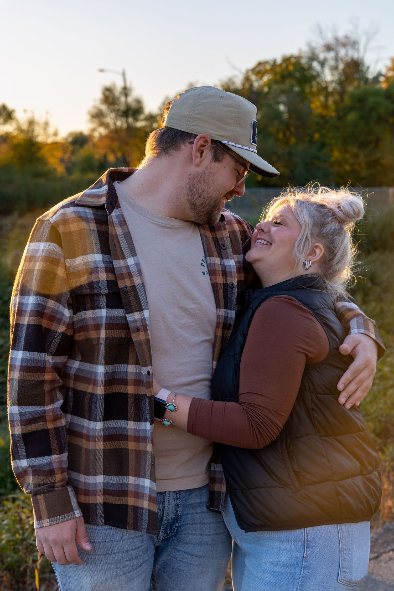 Couple embracing outdoors during golden hour wearing casual plaid and denim.