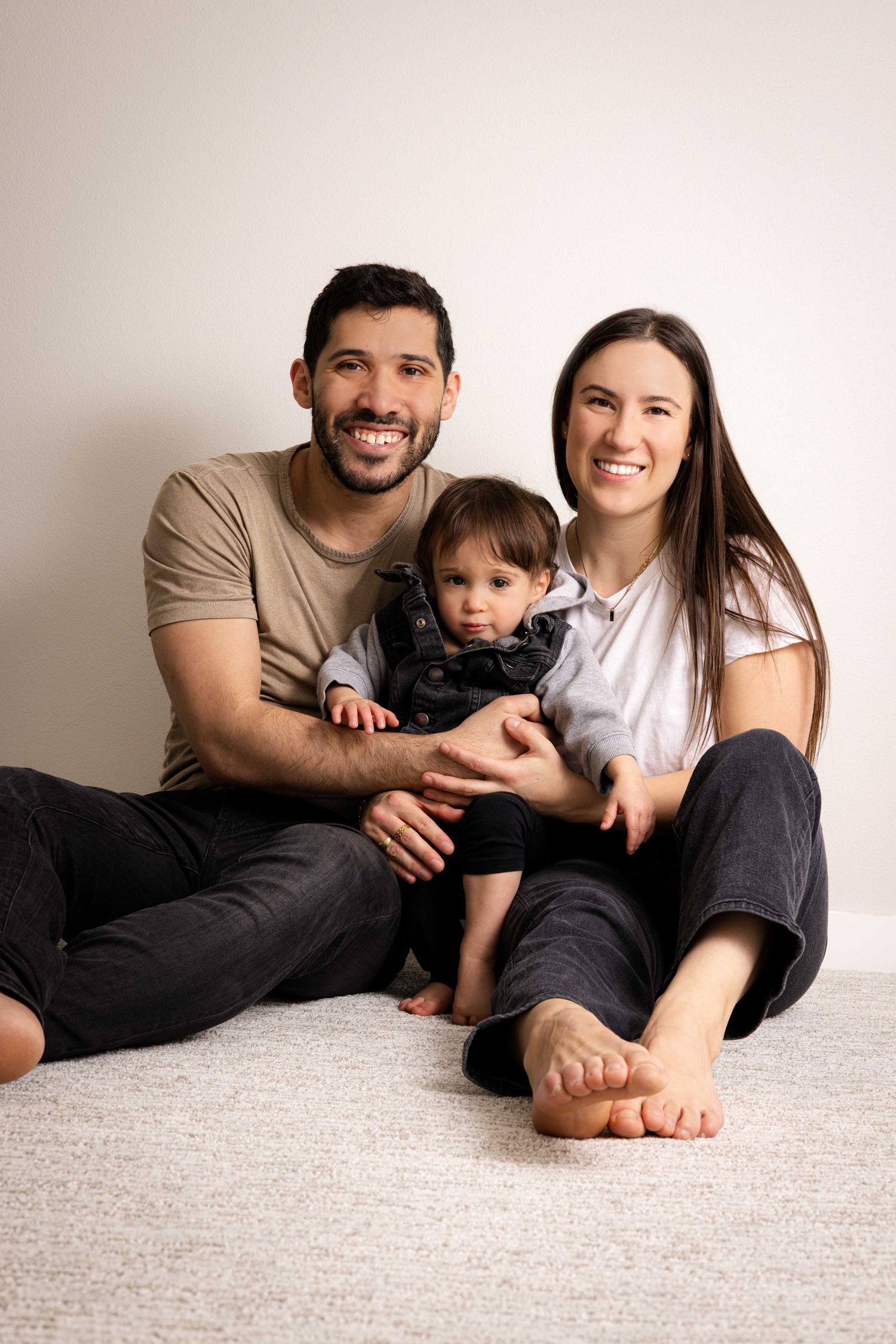 A relaxed family portrait with everyone sitting comfortably on carpet together.