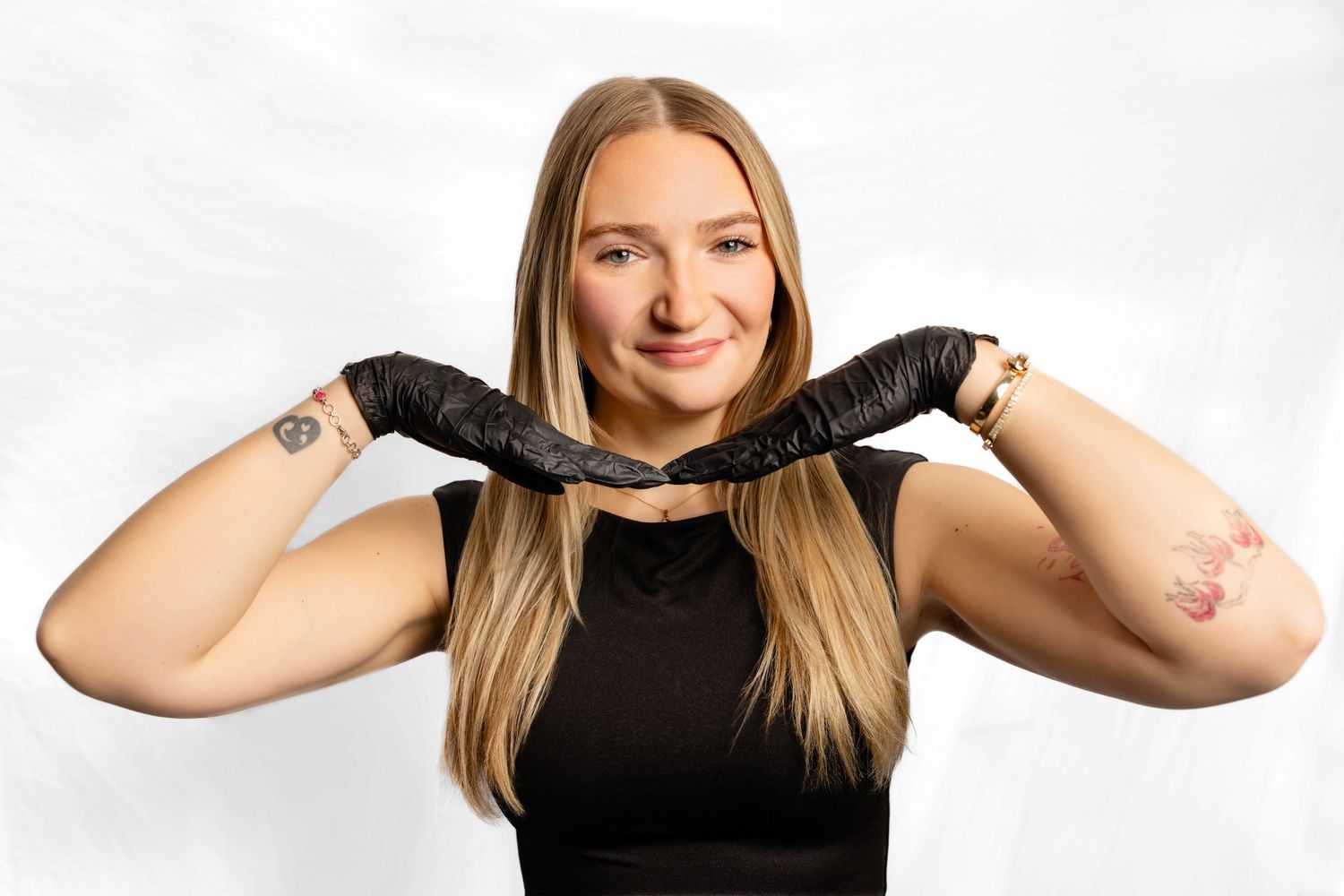 Person in black top holds a braided leather belt against white background, smiling warmly.