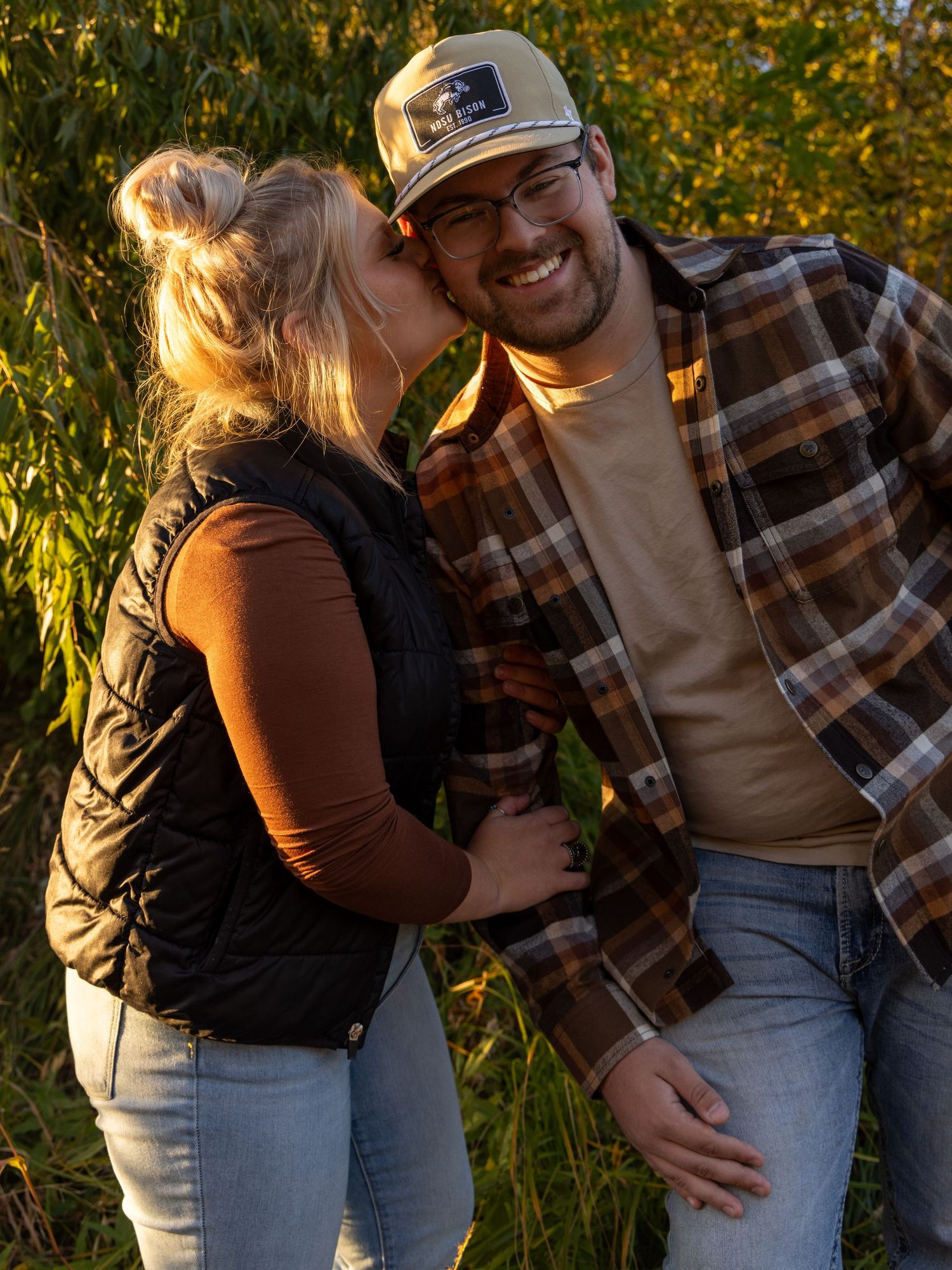 Playful couple photoshoot in golden hour sunlight among tall grass and autumn foliage.