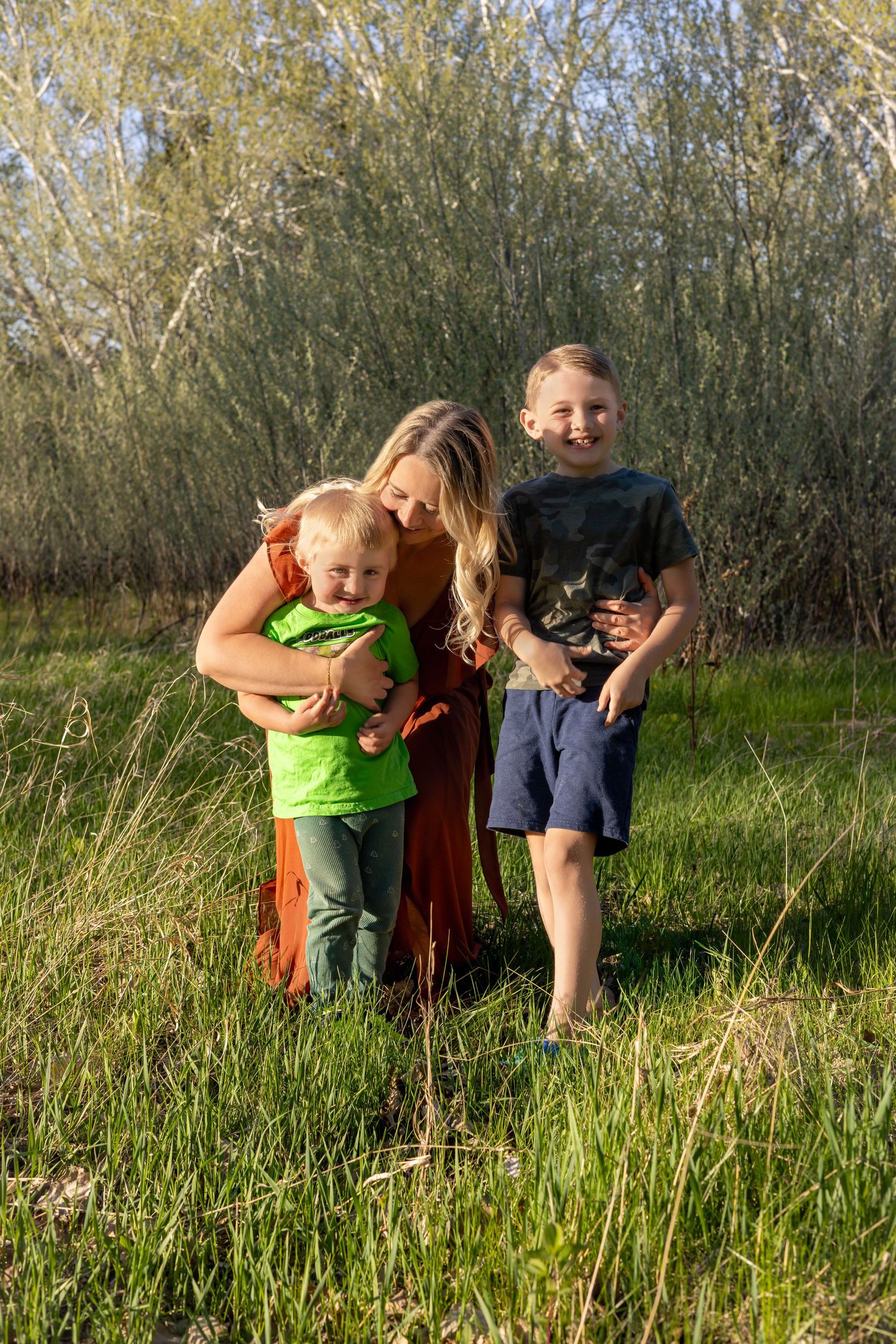 Family sharing tender moment in tall grass field during golden hour.