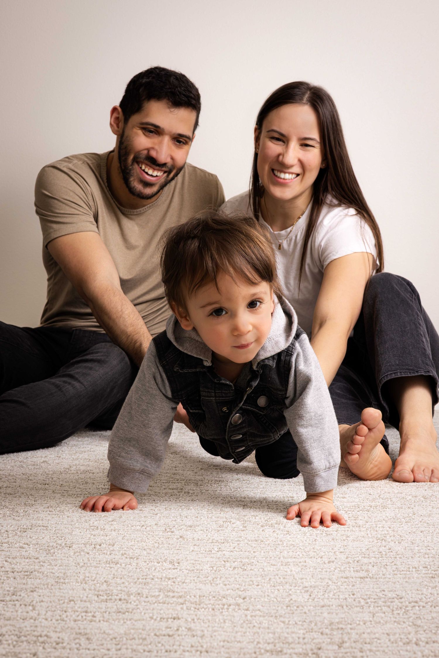 A happy family moment with parents and child playing on carpet together.