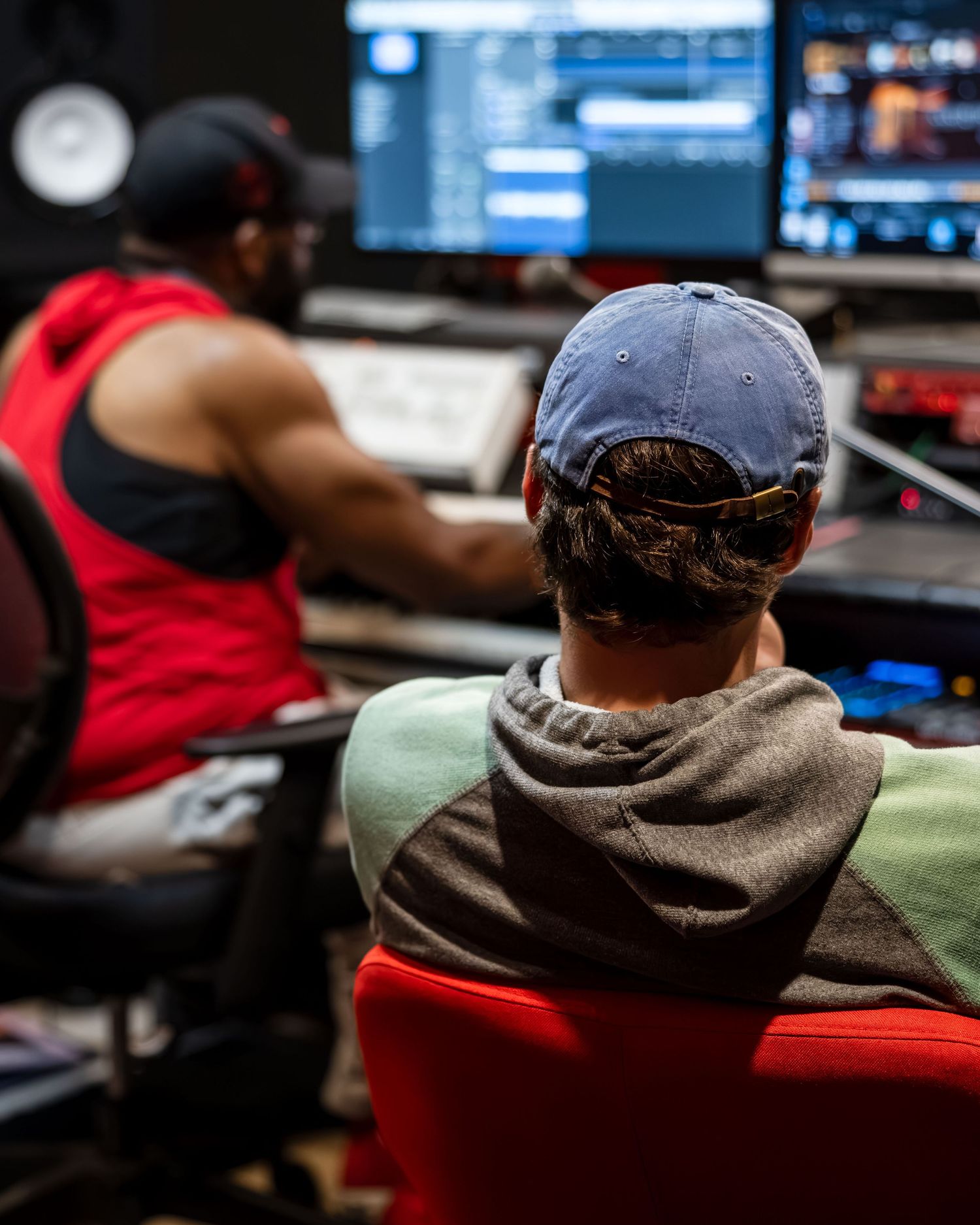 Two music producers collaborating in a professional recording studio with multiple monitors displaying audio software.