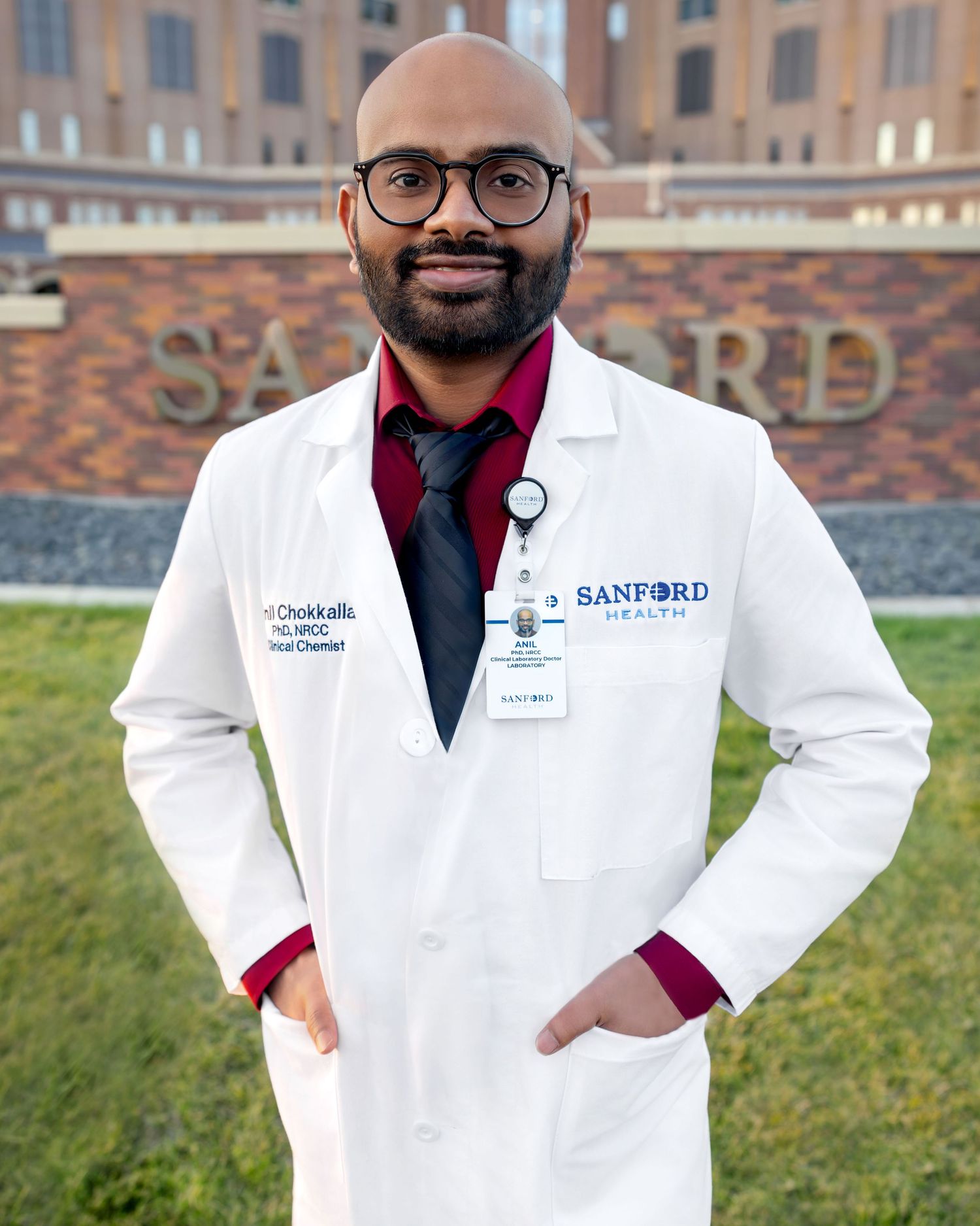 A Sanford Health physician in a white lab coat stands confidently outside the Sanford Health building.