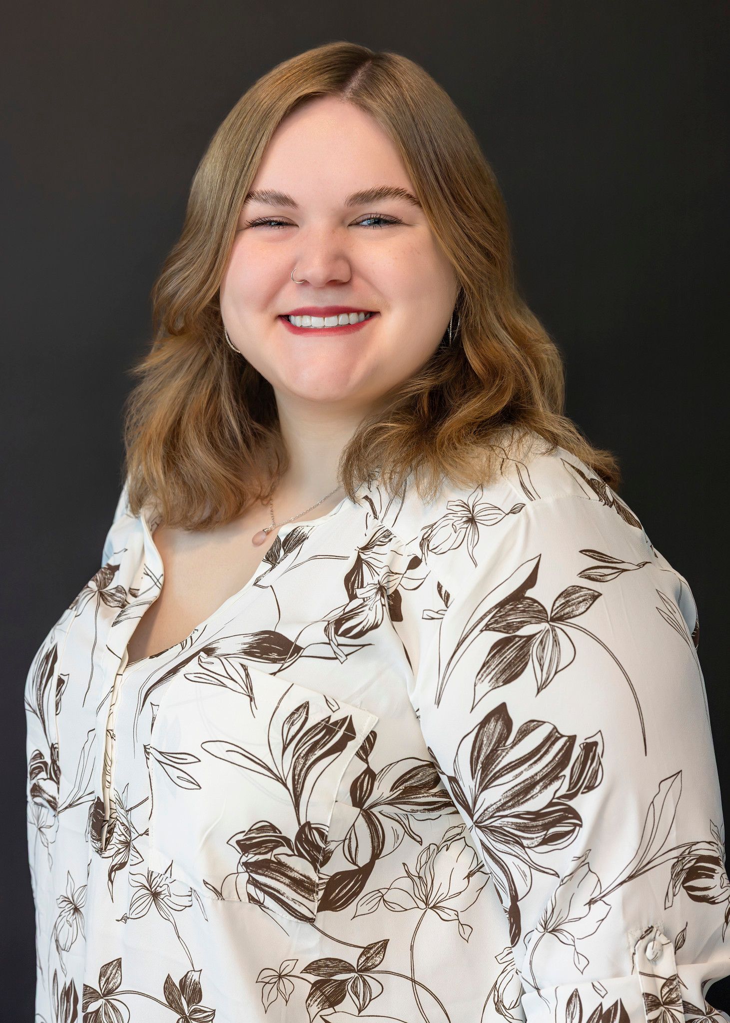 Studio portraits wearing floral print top against dark backdrop.