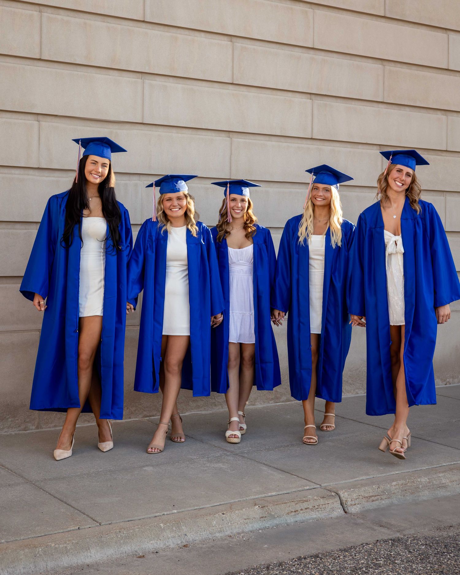 Creative graduation photo showing blue gowns and white shoes lined up against wall.