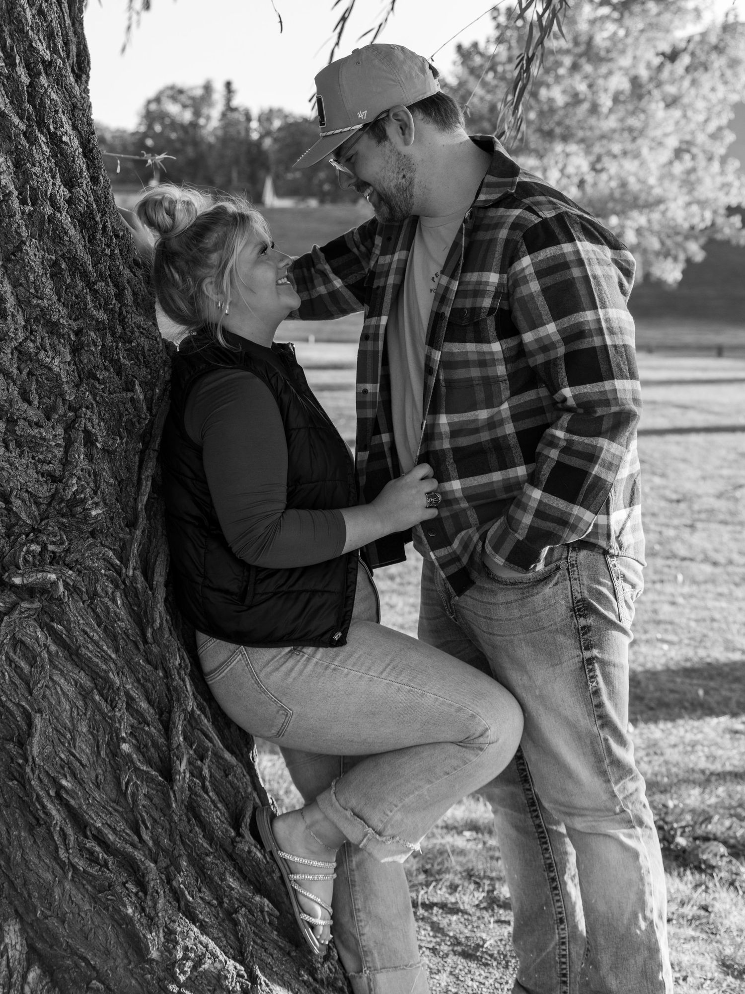 A romantic black and white photo of a couple sharing an intimate moment against a tree trunk.