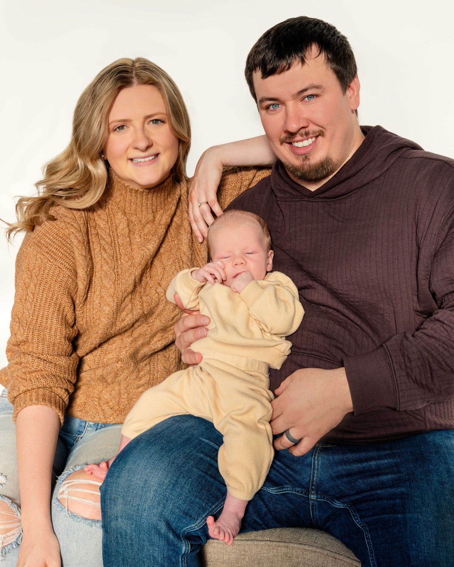 Casual family photo session showing parents with their newborn on a light background.