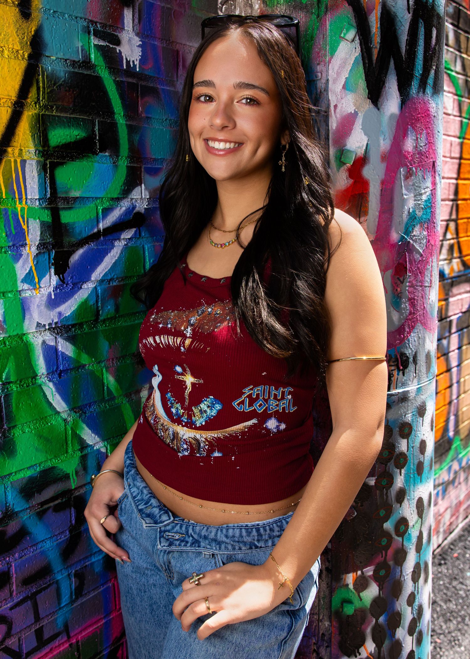 Smiling young woman in red graphic crop top and jeans poses against colorful graffiti wall.