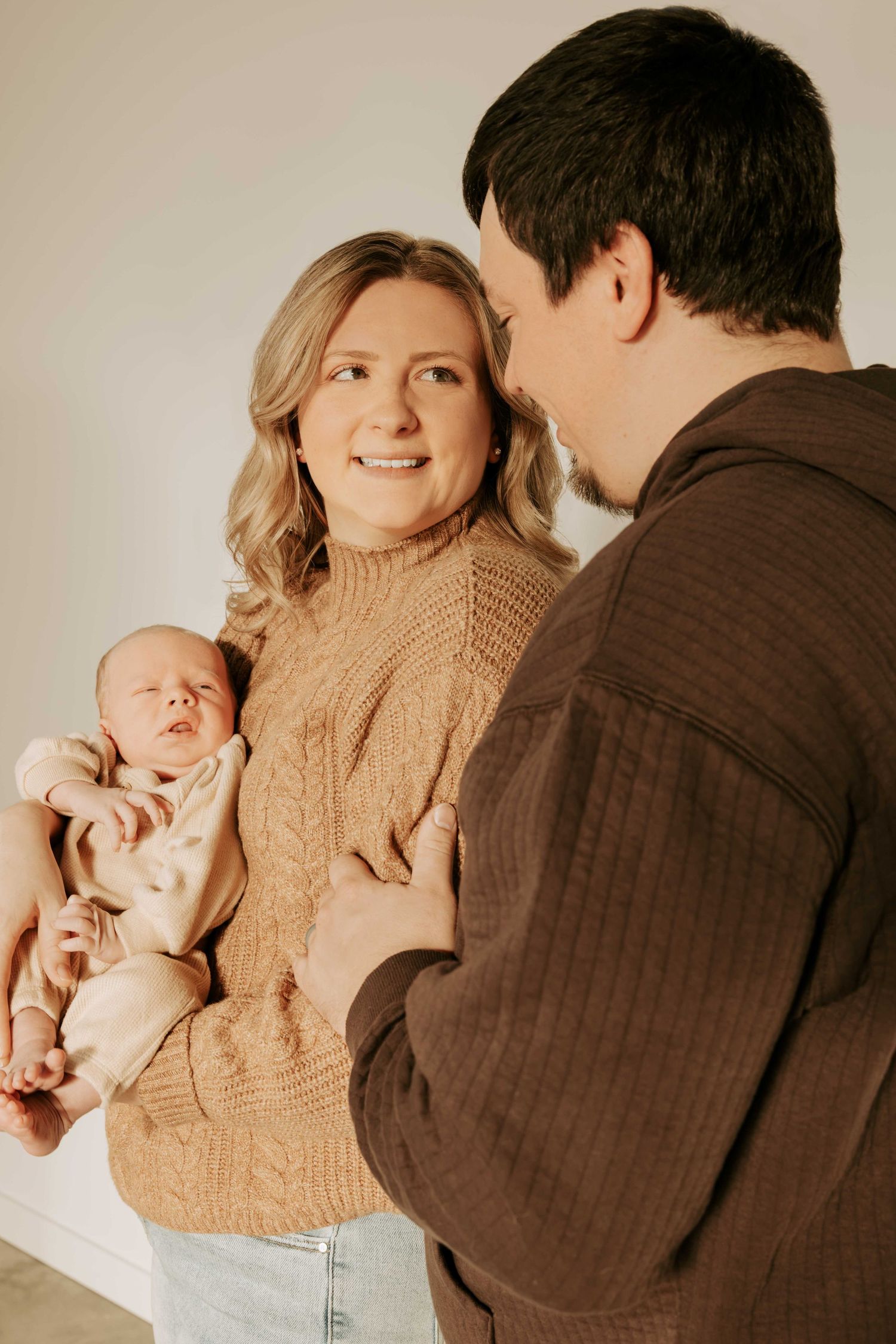 Family portrait in warm tones featuring a baby in a cozy sweater setting.