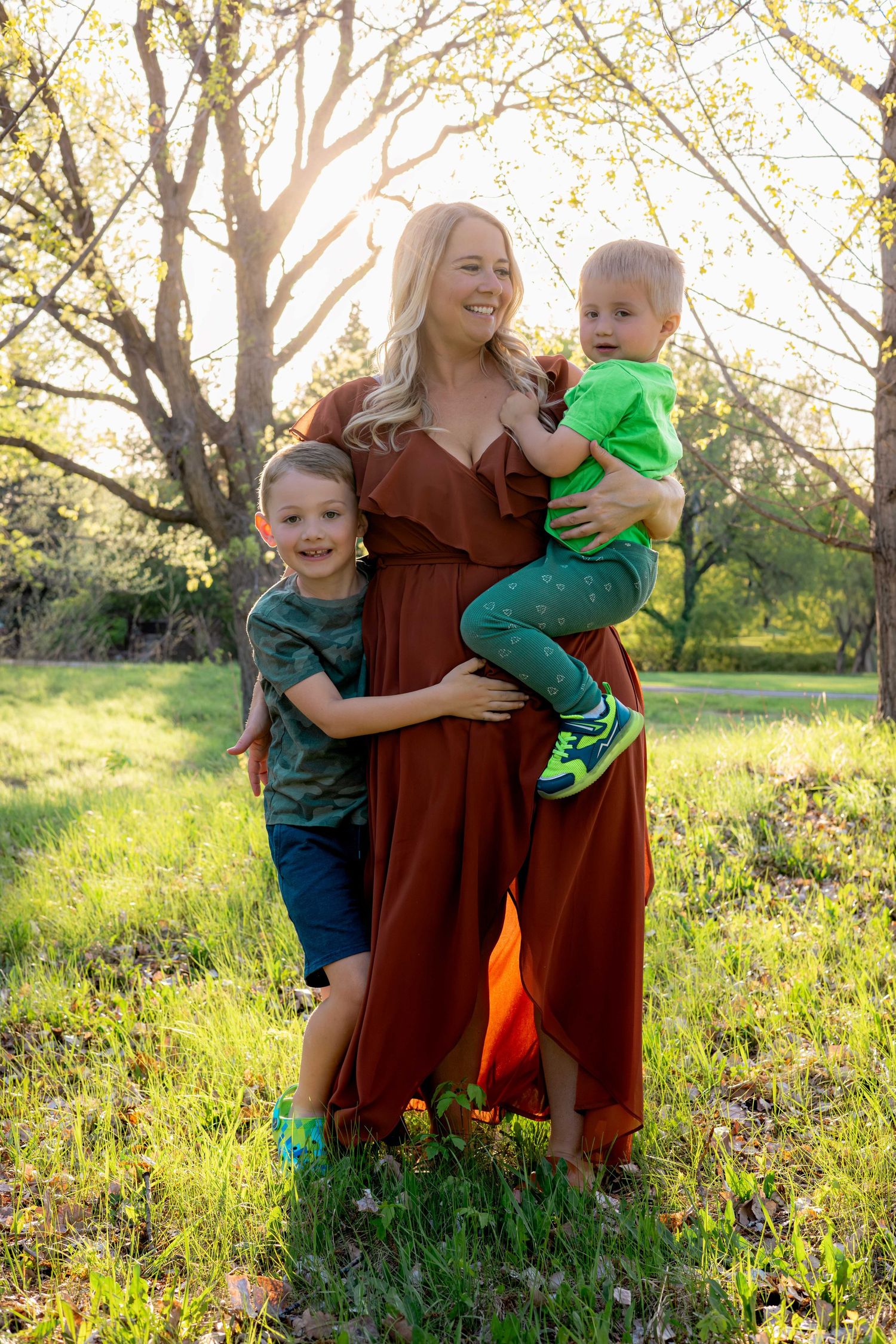 Joyful outdoor family photoshoot in a meadow during golden hour with a rust-colored dress.