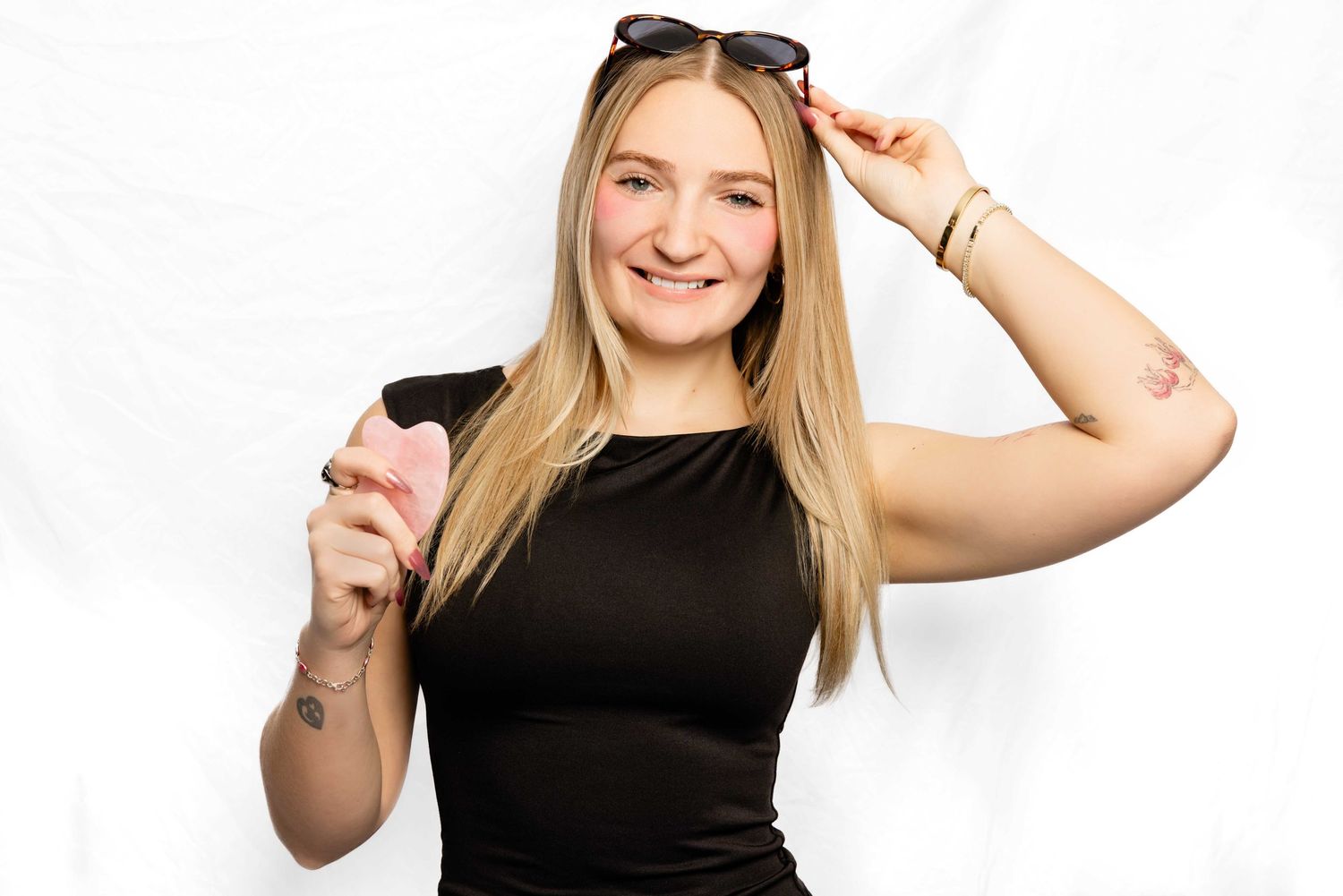 A person in a black sleeveless top holds sunglasses and poses against a white background.