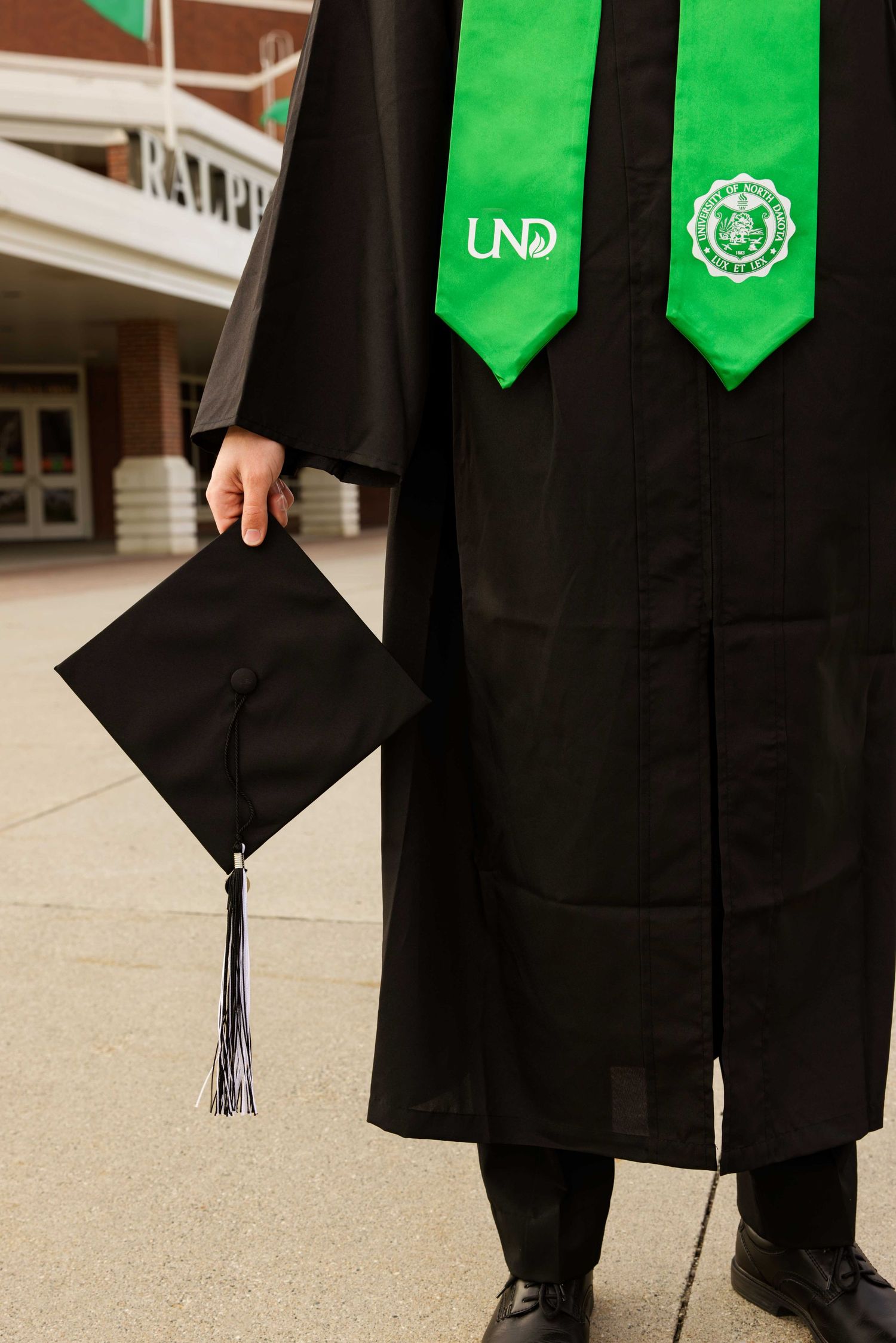 Graduation cap and green UND stoles shown against black graduation gown.