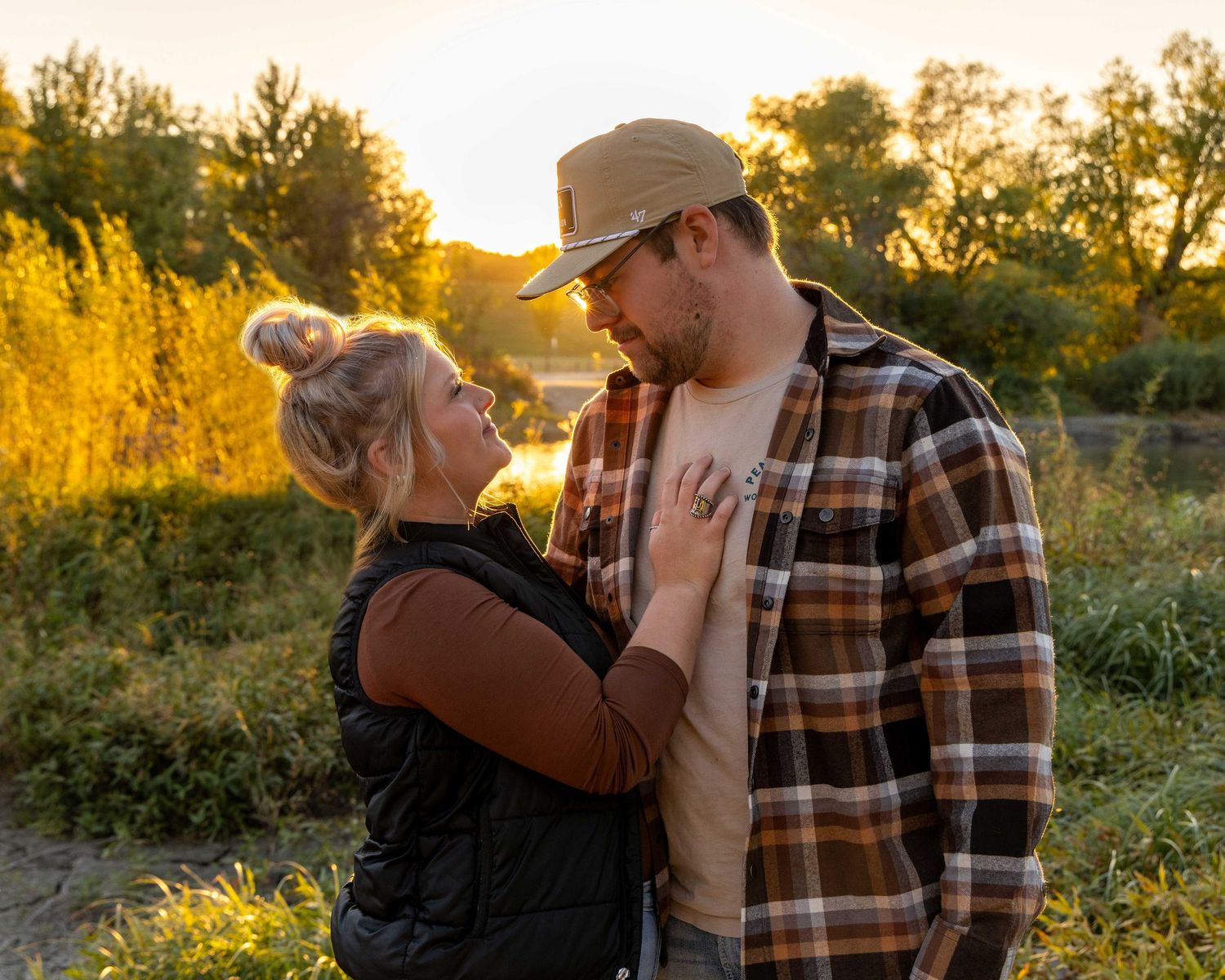 Couple shares intimate moment at sunset in rural field with golden light.