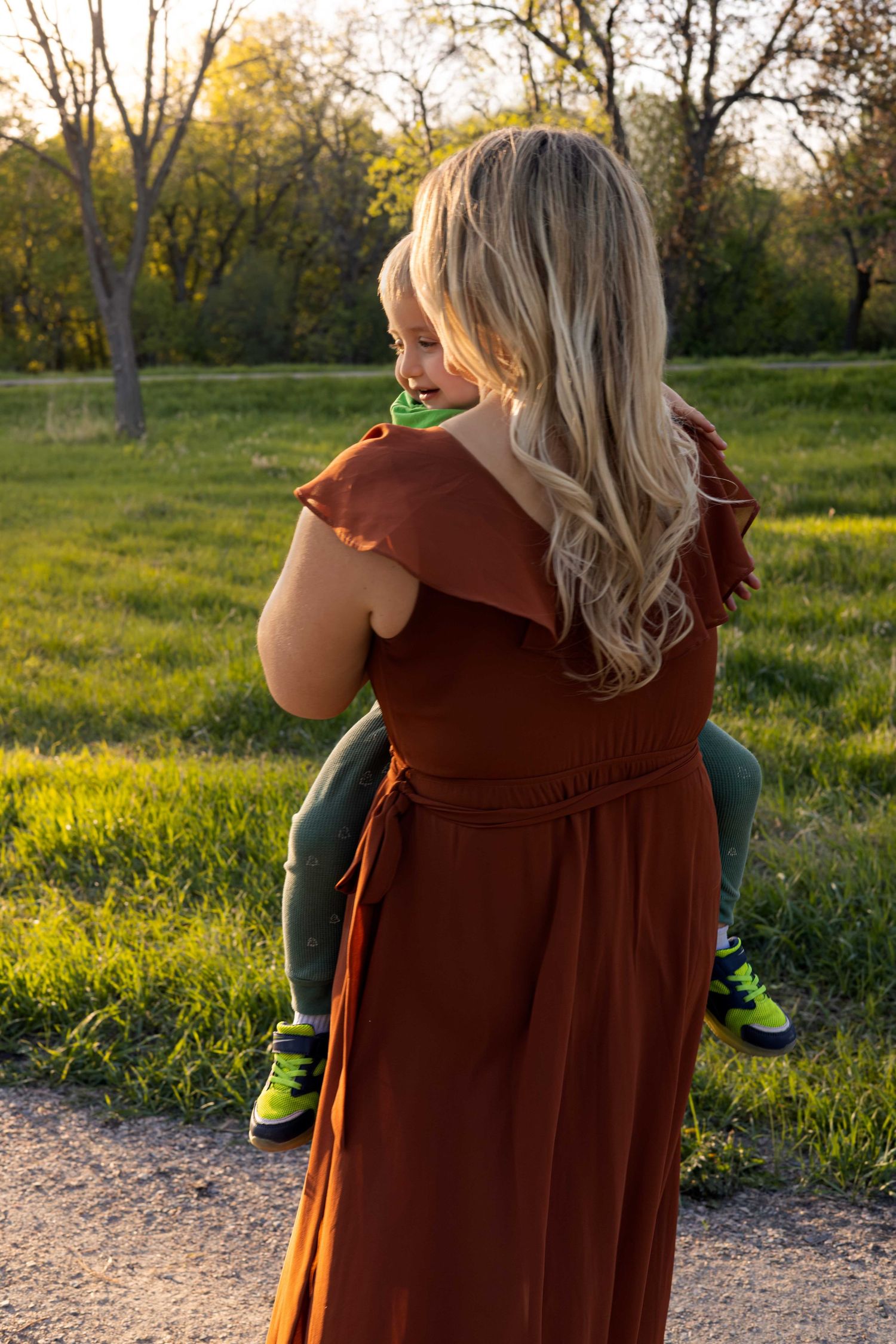 Walking along a sunlit path wearing a flowing rust-colored dress during golden hour.