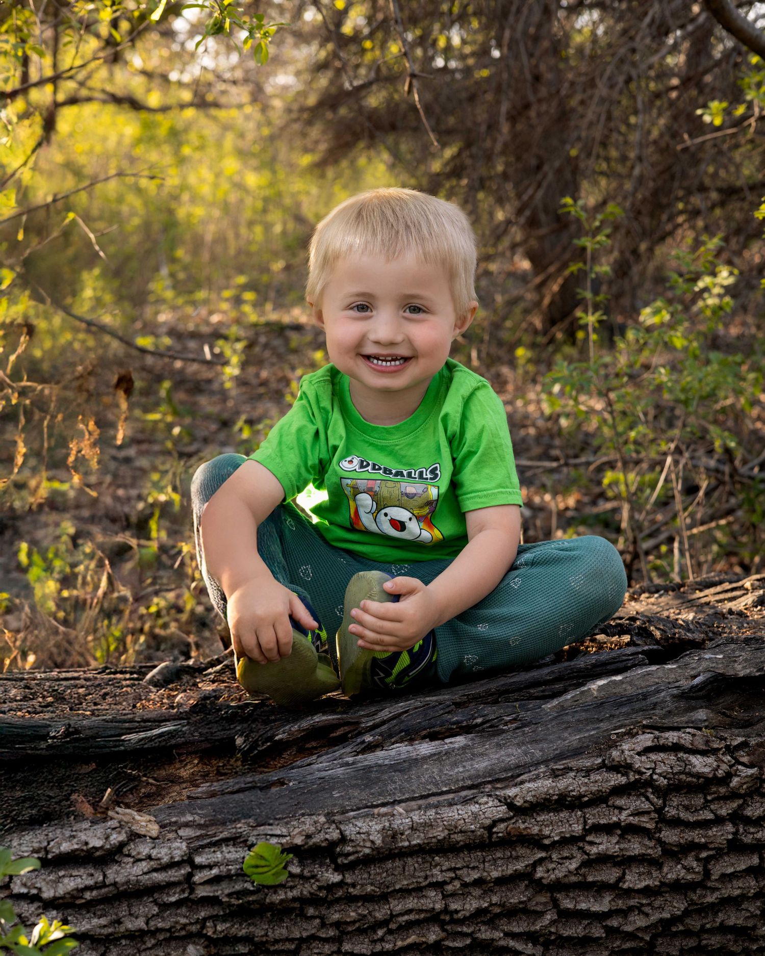 Child lying playfully on large fallen tree trunk in forest setting.