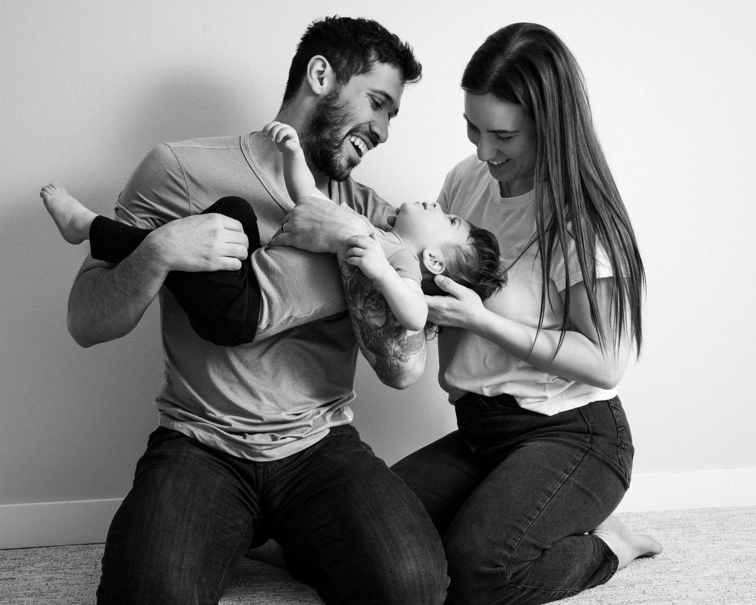 A playful family moment captured in black and white as they laugh together on the floor.