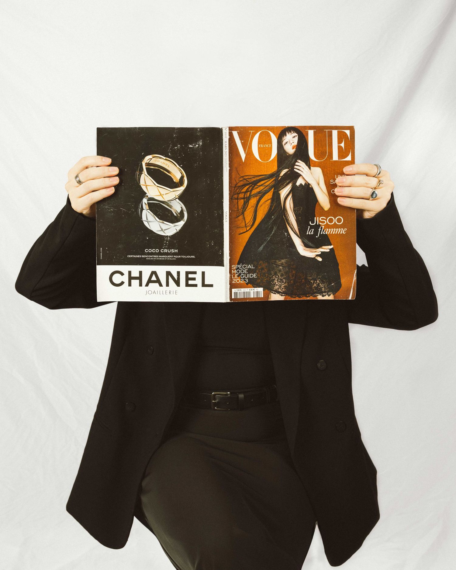 Person in black holding up fashion magazine covers and Chanel branding materials.