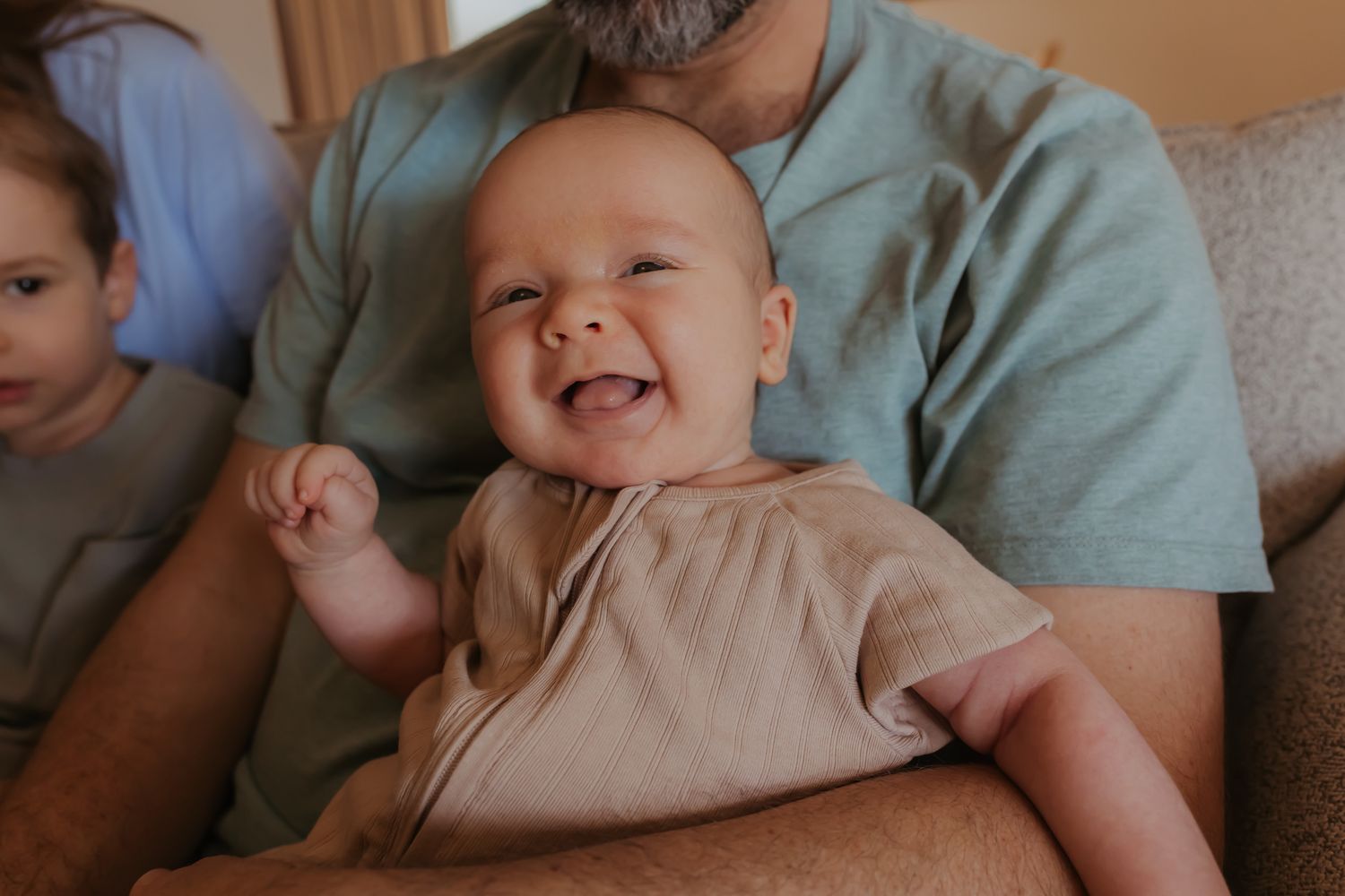 A baby smiles while being held and rocked in someone's arms wearing a mint green shirt.