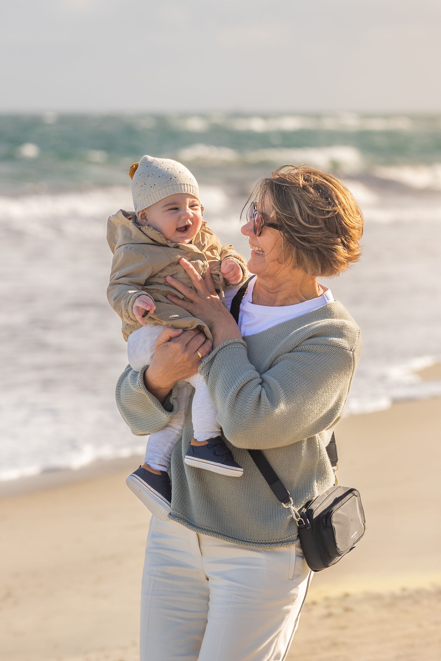 A tender moment shared between parent and child playing on a sunny beach with ocean waves in the background.
