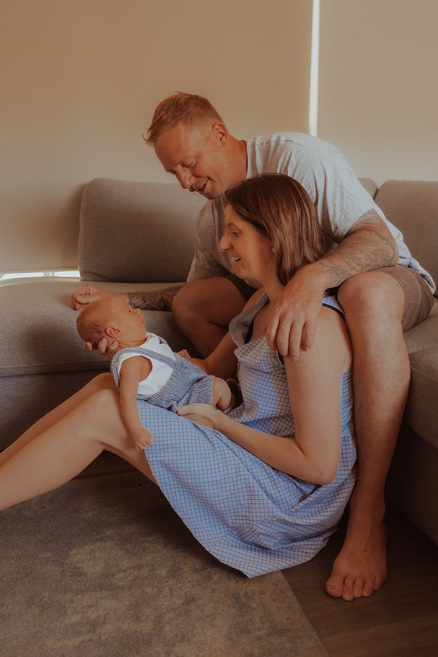 A family shares an intimate moment together while relaxing on a gray couch in warm lighting.