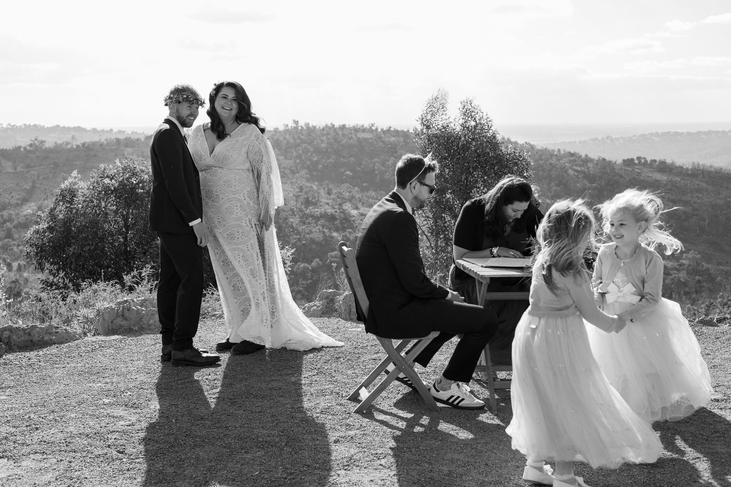 A wedding couple and their wedding party walk together through a scenic outdoor landscape at sunset.