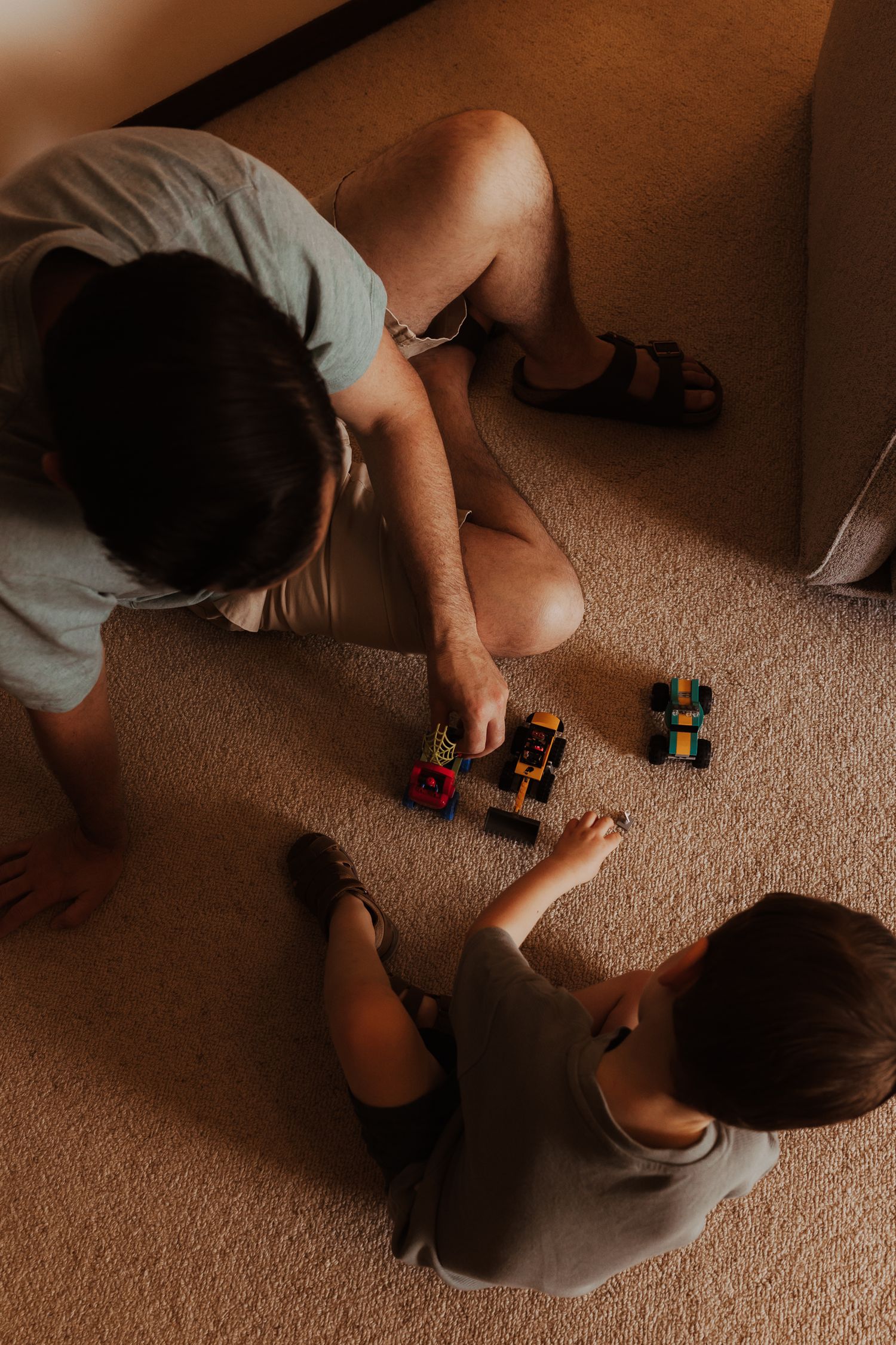 Children playing with colorful toy cars and blocks on a beige carpet in a dimly lit room.