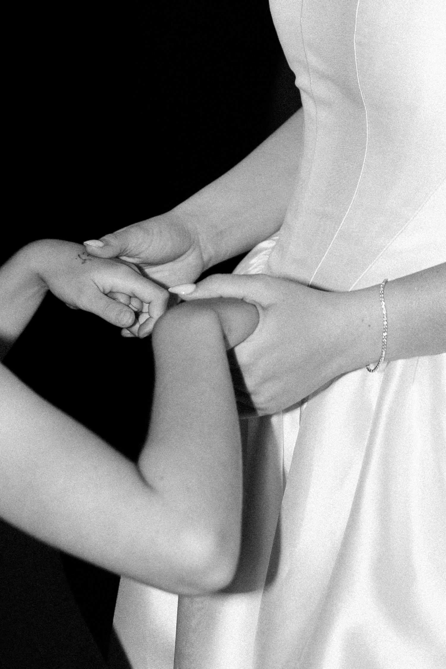 A series of black and white close-up photos showing hands holding and adjusting fabric details on a white dress.