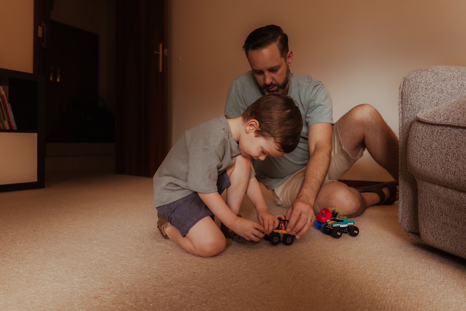 Two people sit on carpet playing together with video game controllers near a couch in a living room.